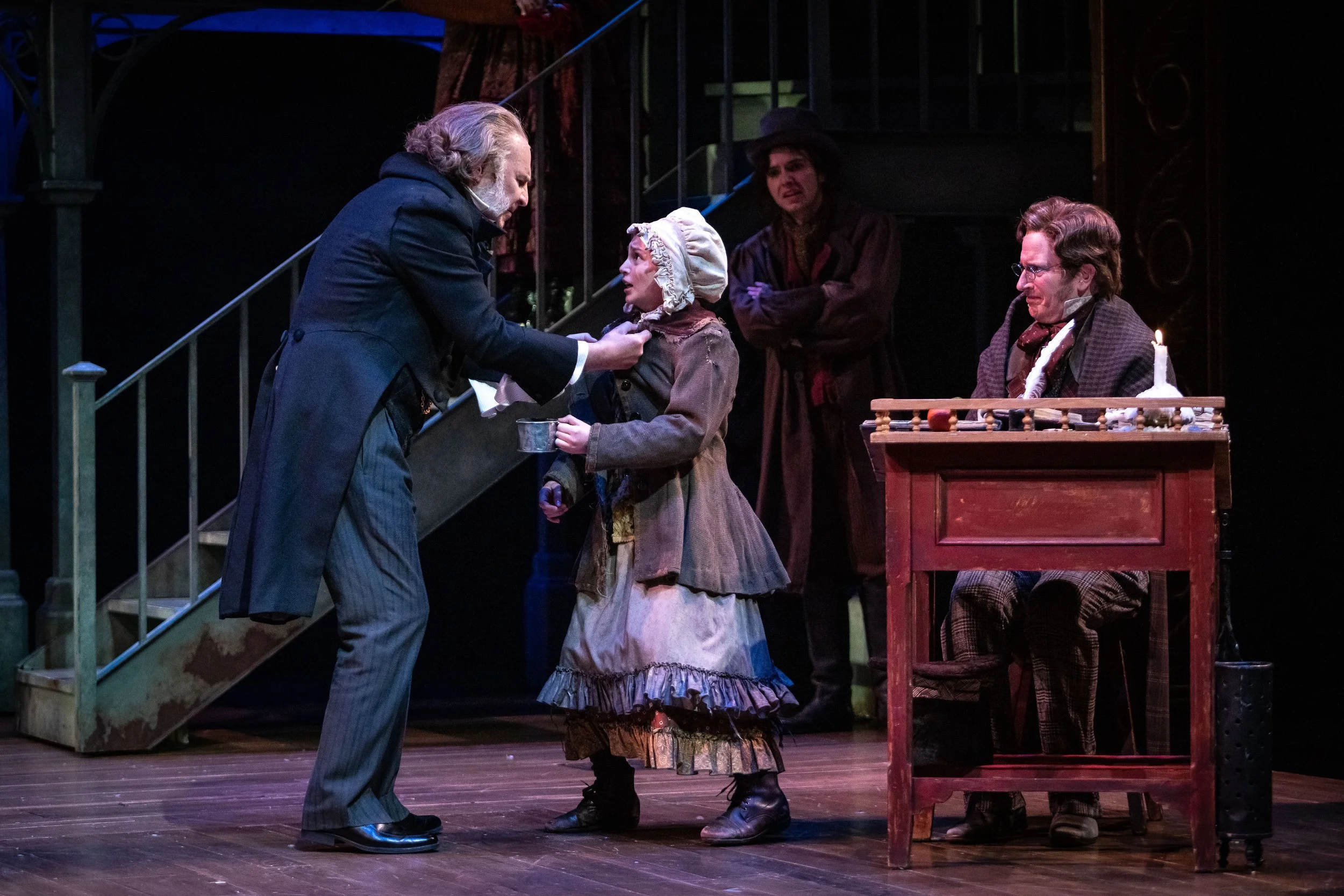 A theatrical scene from A Christmas Carol at The Denver Center for the Performing Arts with Beggar Child, Ebenezer Scrooge, and Bob Cratchit, at Scrooge's office