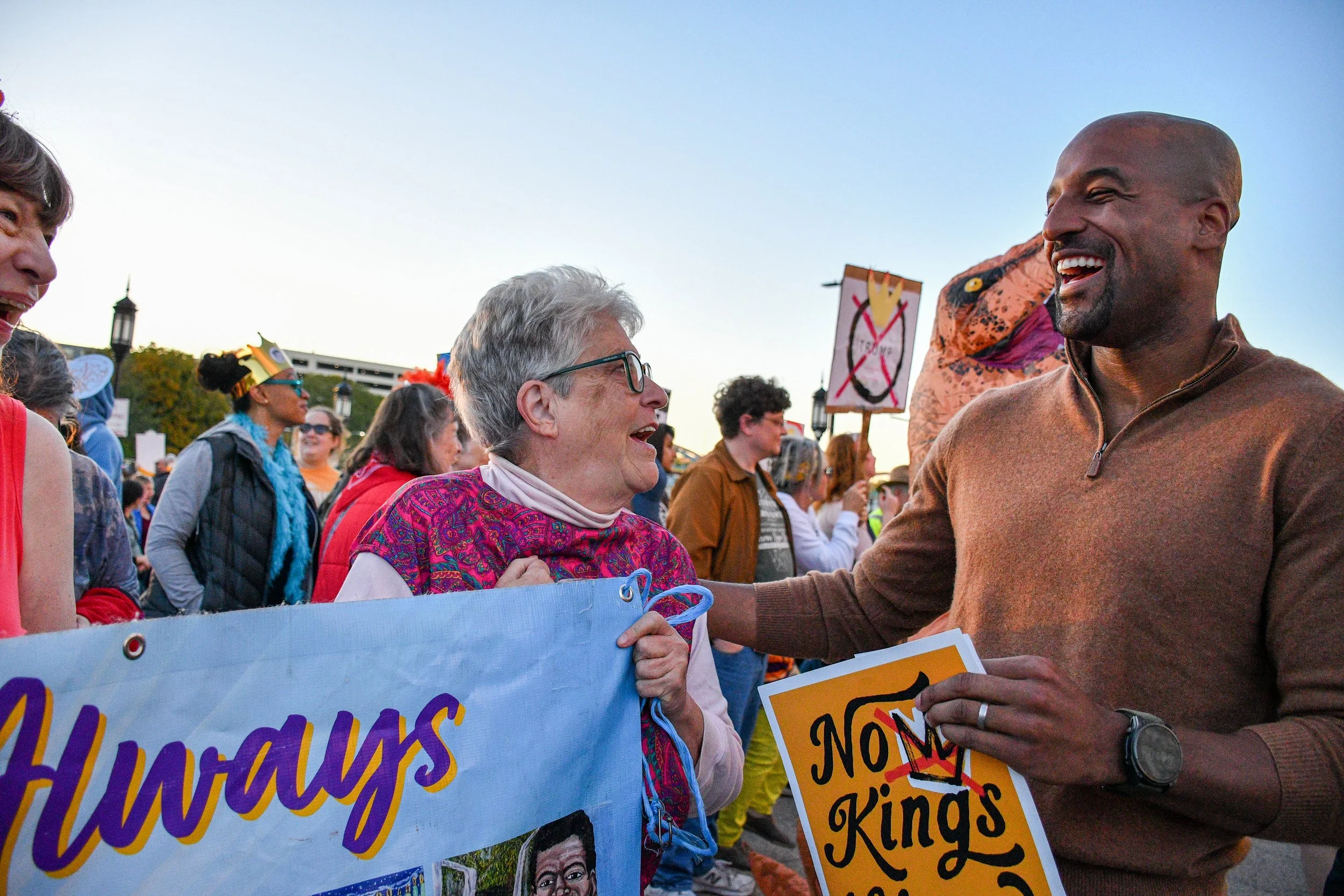 Mark and an older woman smiling and talking at a No Kings Protest, surrounded by a crowd holding signs.