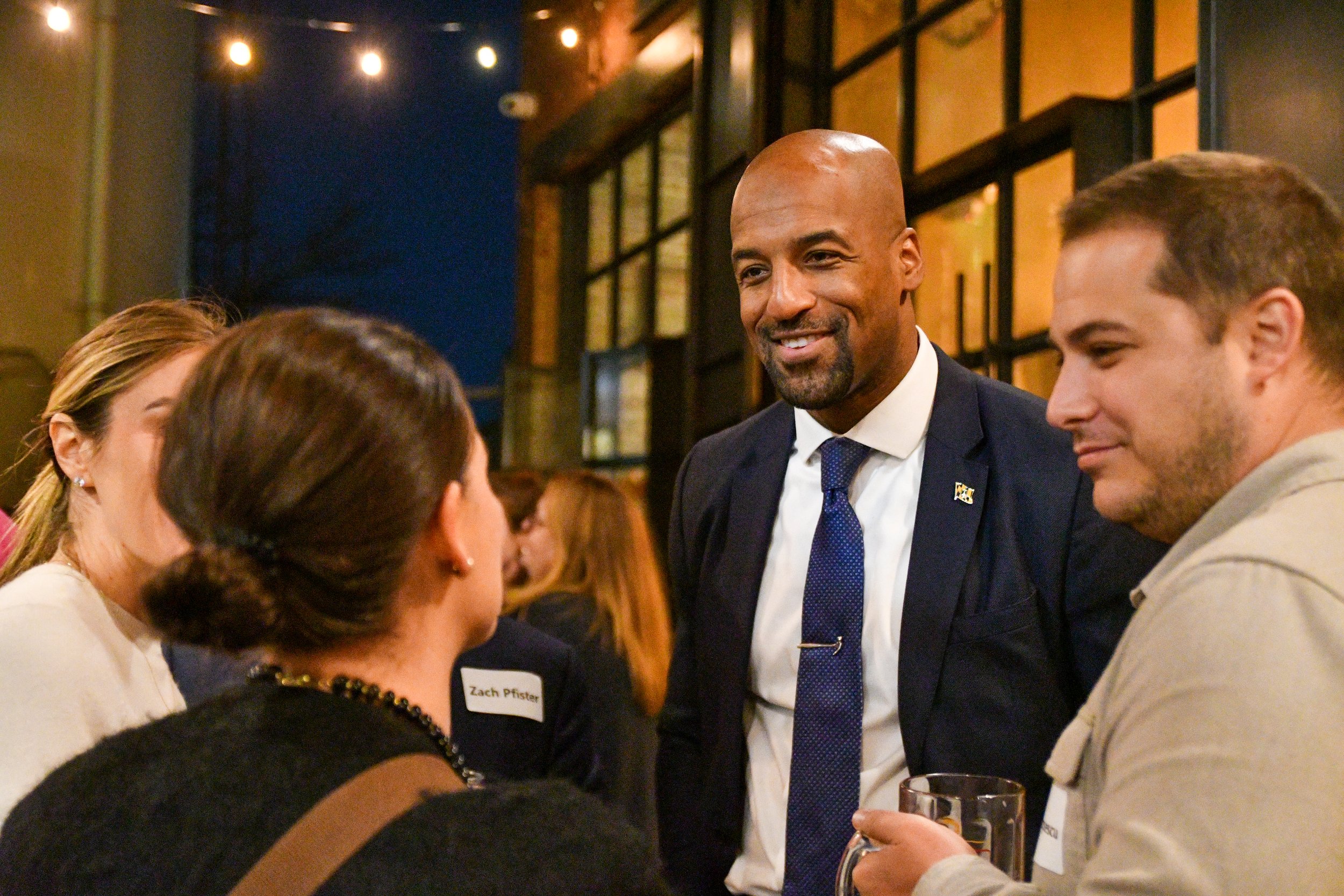 Mark engaged in conversation with two people, one man and one woman, in a social gathering setting.