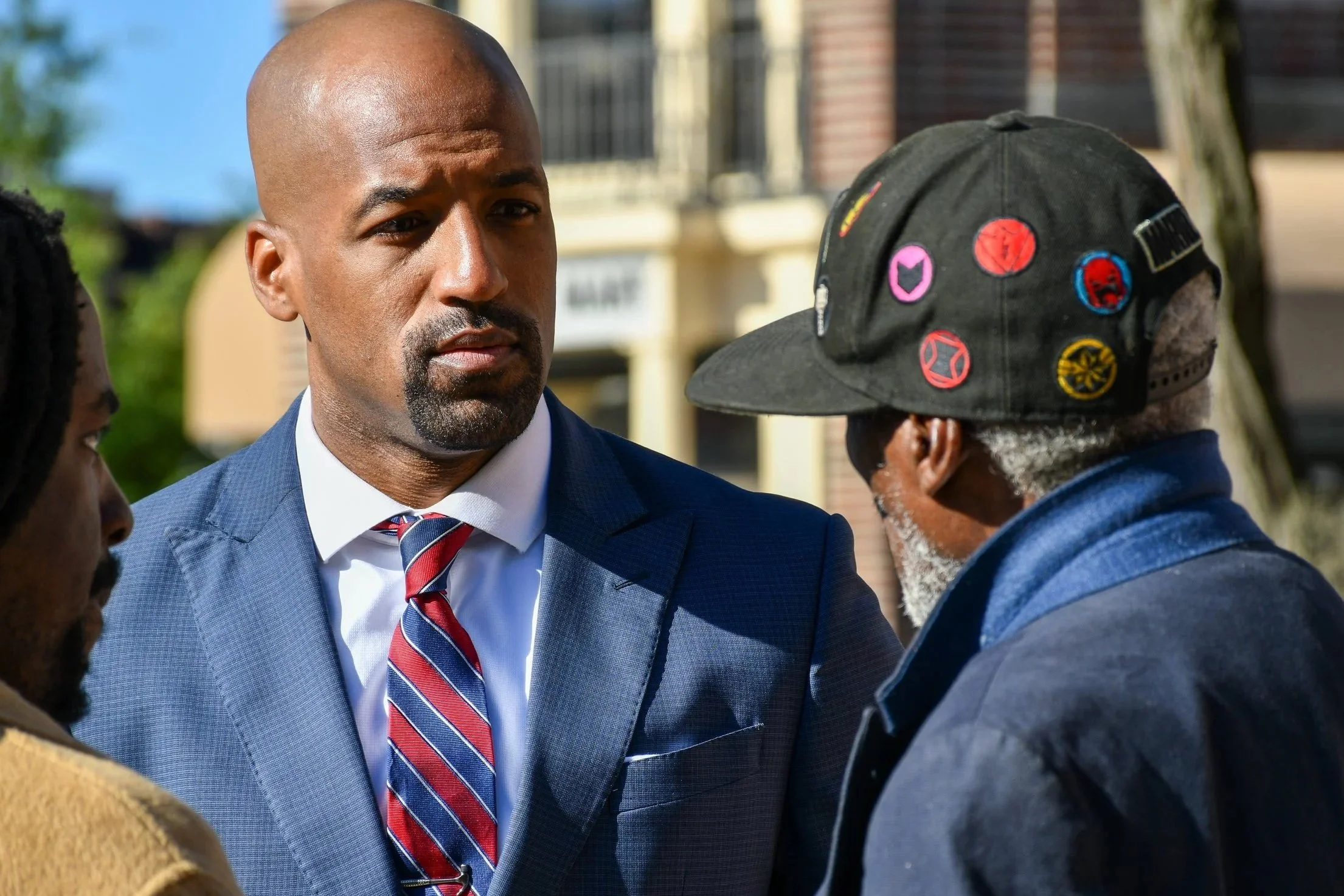 Mark engaged in a serious conversation outdoors with two older men facing him.