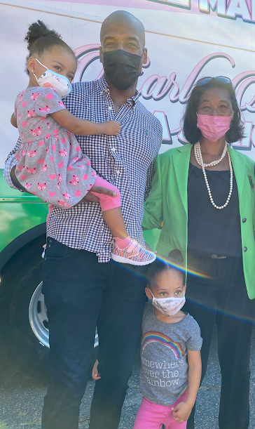 Mark holding his daughter girl in pink and gray clothing and a mask next to a bus.
