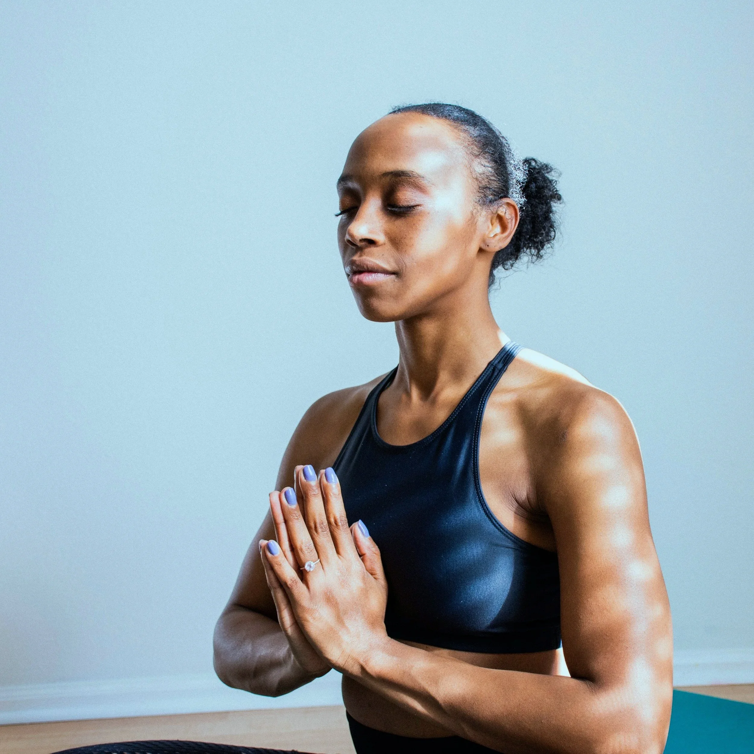A woman with closed eyes practicing yoga with hands in prayer position, indoors.