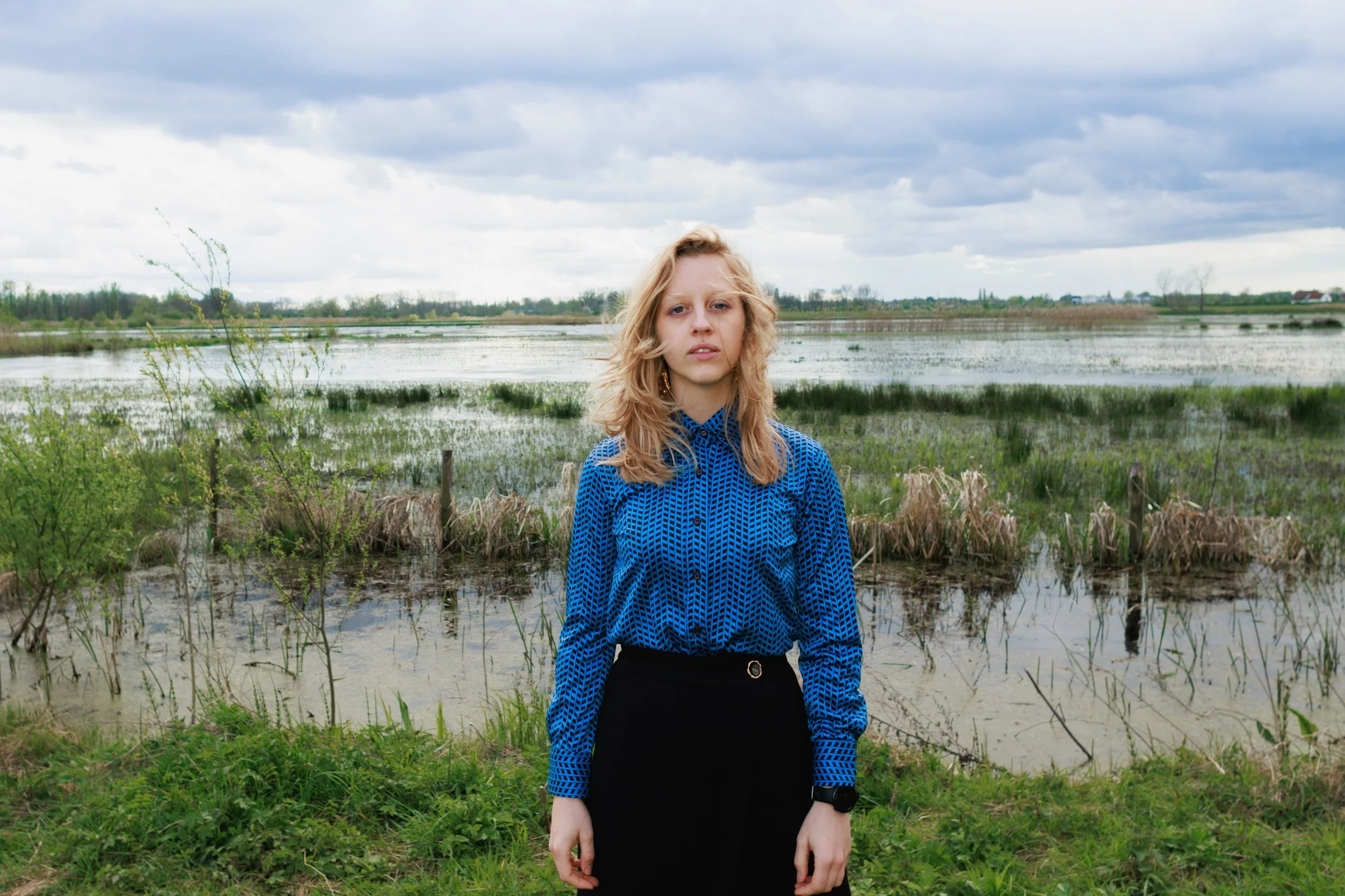 A striking portrait of a girl in Ghent, her blue shirt providing a beautiful color contrast against the natural green background of the Bourgoyen in 2024.