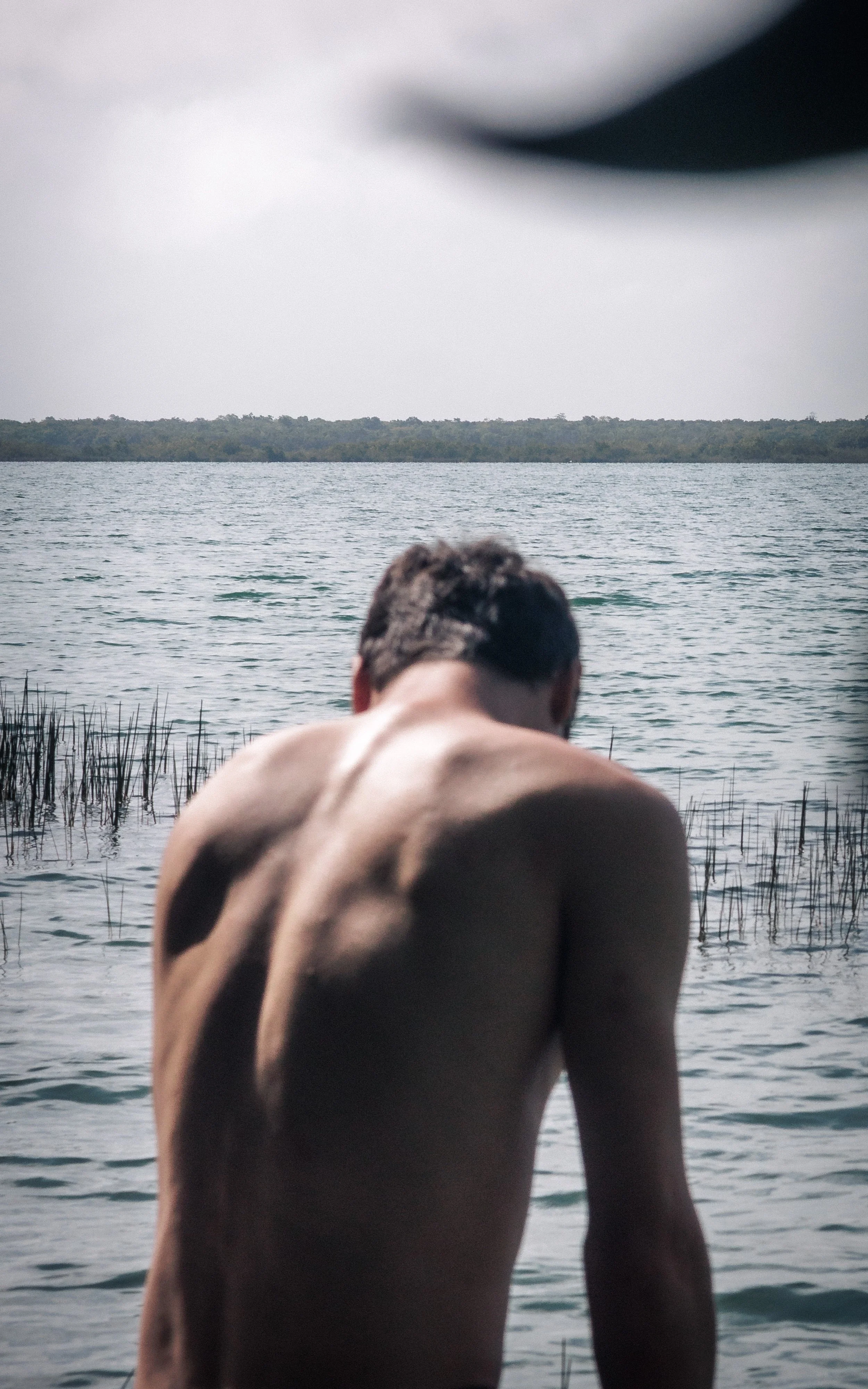 An atmospheric photograph of my boyfriend, intentionally blurred as he sits by the serene edge of a lake in Bacalar, Mexico.