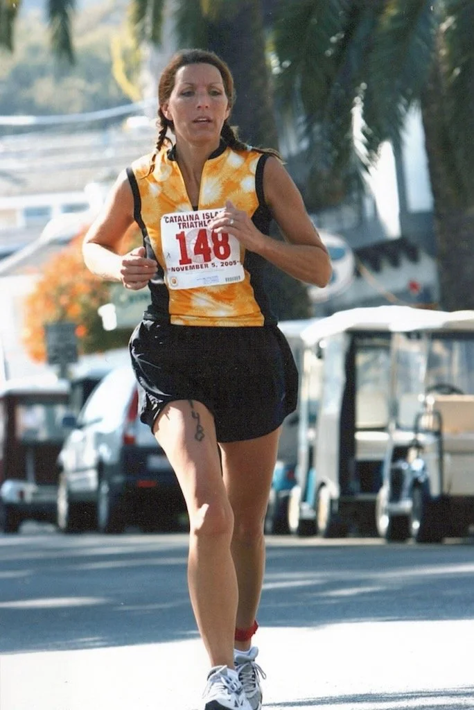 Female runner with bib number 146 participating in a triathlon event, running outdoors on a sunny day with palm trees and parked golf carts in the background.