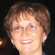 Close-up of a smiling elderly woman with short, light brown hair, wearing glasses and earrings, in an outdoor setting at night.