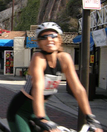 Carolyn Cooper wearing a helmet and sunglasses riding a bicycle outdoors, smiling.