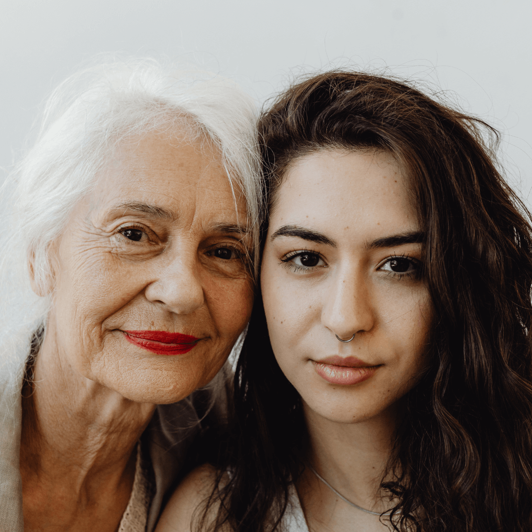 Close-up of an elderly woman with white hair and a young woman with dark wavy hair, both smiling gently and posing together.