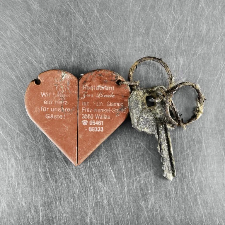 A rusted key attached to a red heart-shaped paper with printed text on it.