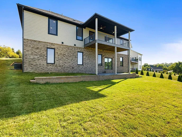 Modern two-story house with brick and siding exterior, large windows, balcony, and a spacious grassy backyard.