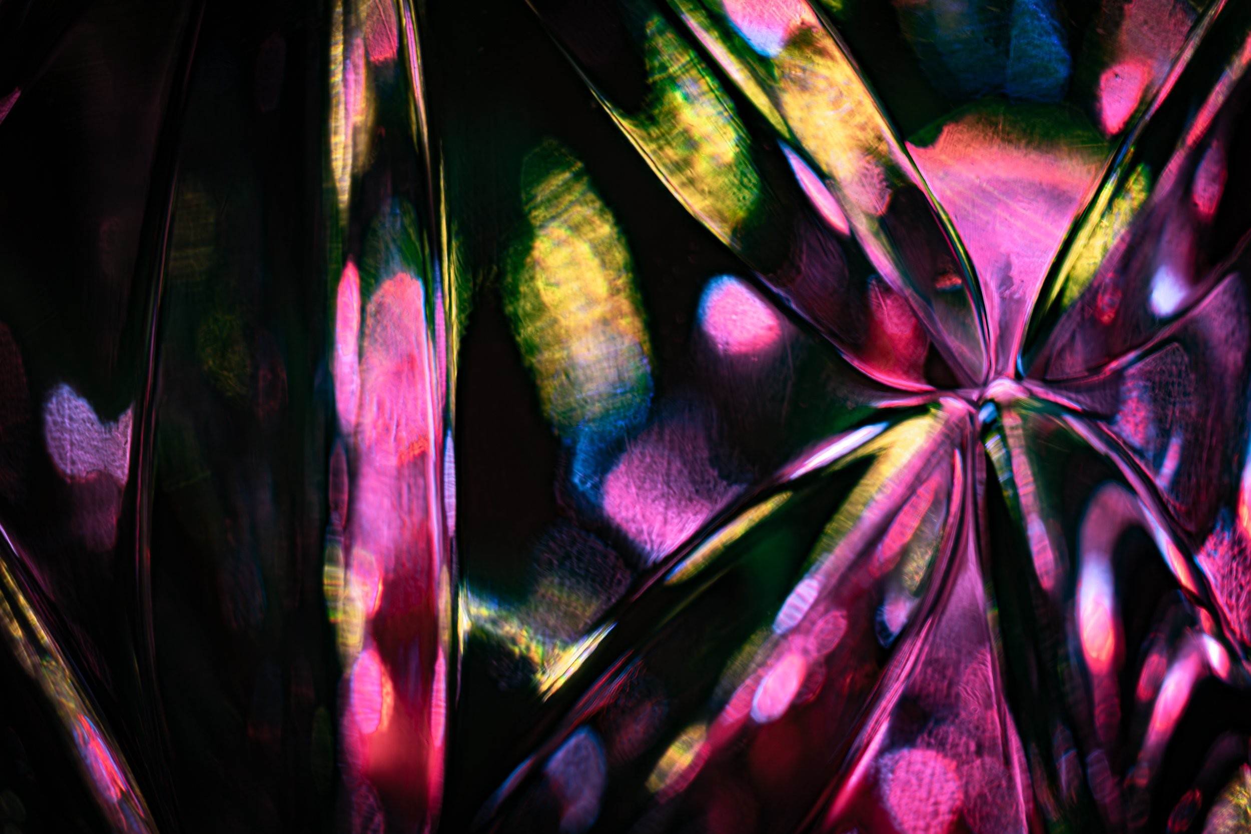 Close-up of colorful, reflective, iridescent surface with bright pink, green, blue, and purple hues creating abstract patterns.