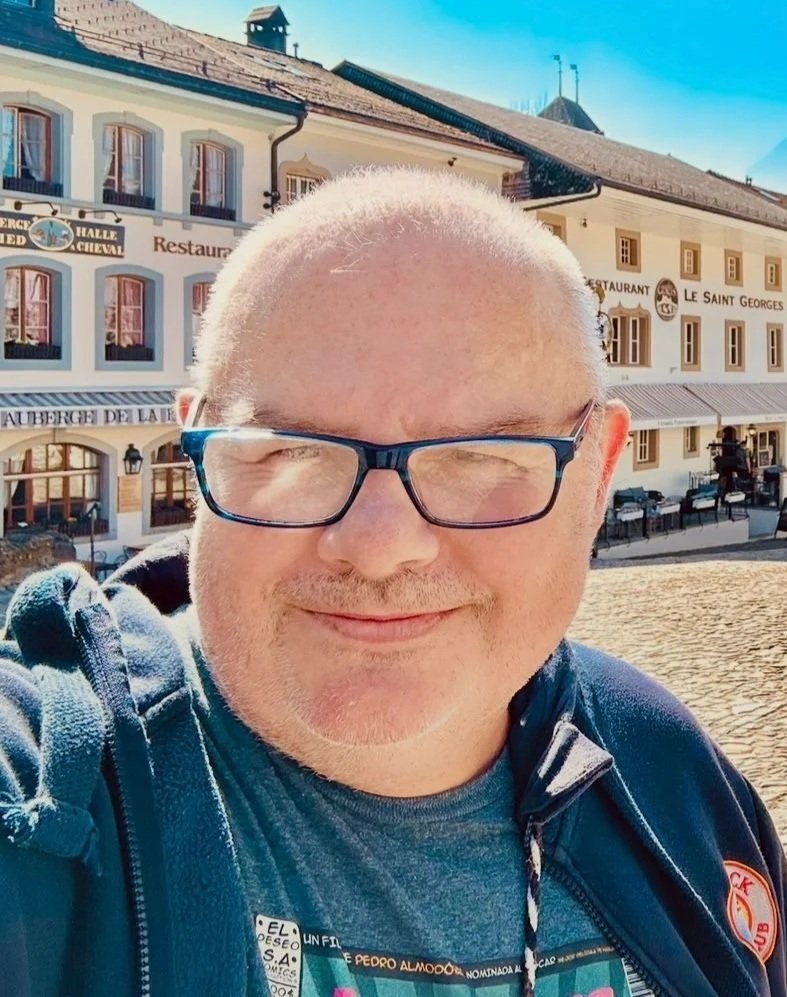 Man wearing glasses, and a navy hoodie, standing outdoors.