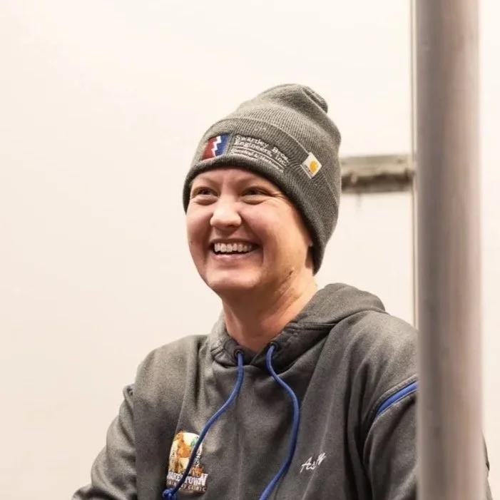 A smiling woman wearing a gray beanie and a gray hoodie.