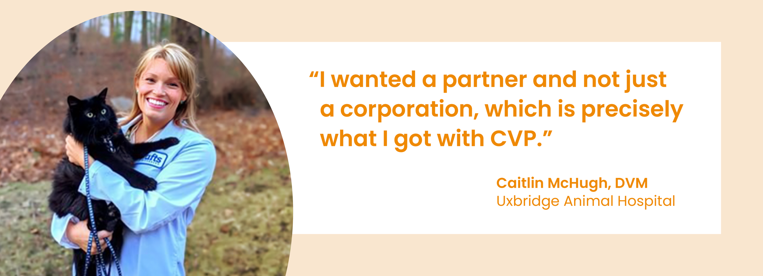 A woman with blonde hair, wearing a light blue jacket, holding a black cat outdoors in a forested area with leaves on the ground.