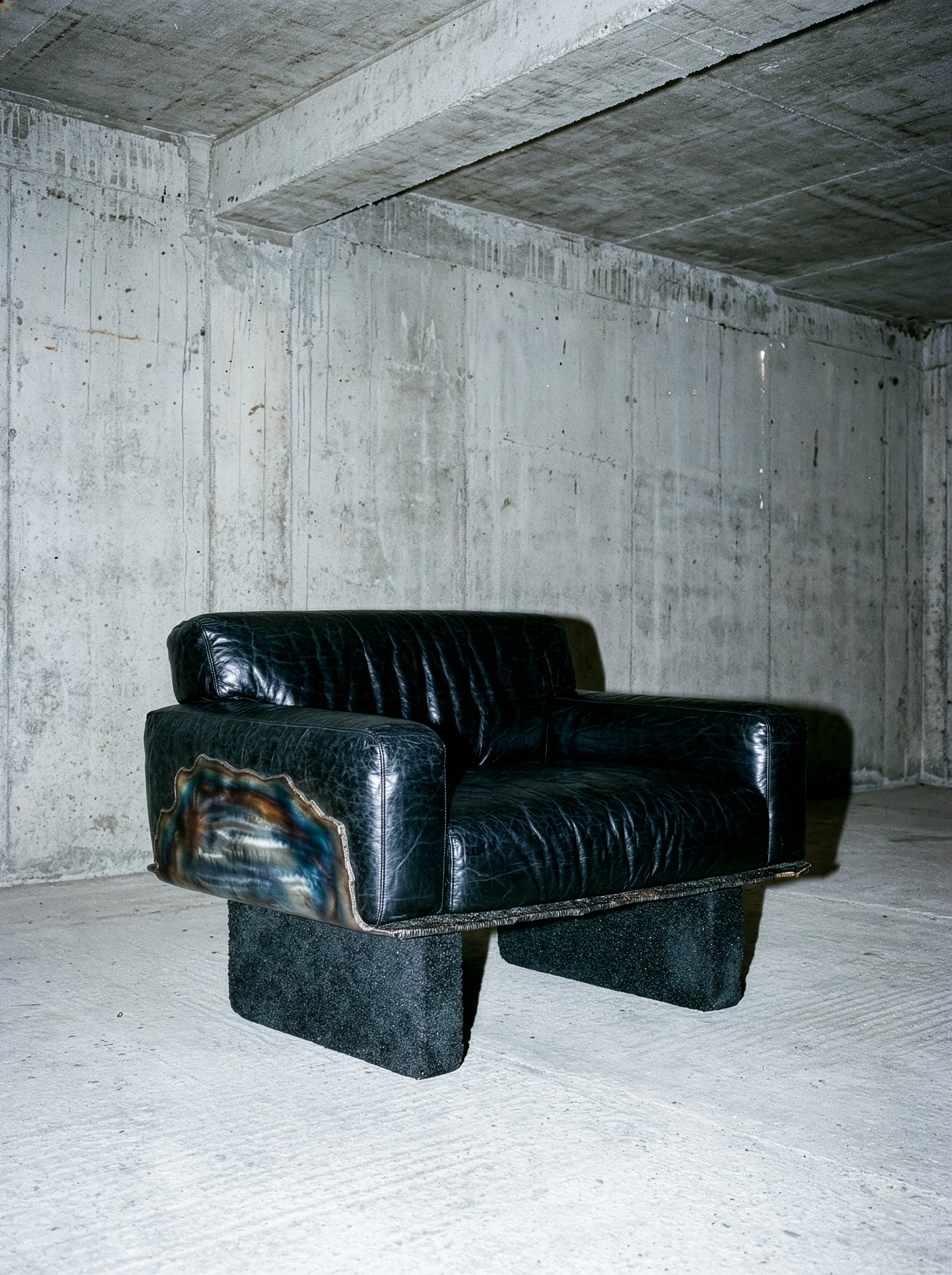 Canapé en cuir noir placé sur un sol en béton dans une pièce sans décoration avec murs en béton.  PAUL HARDY