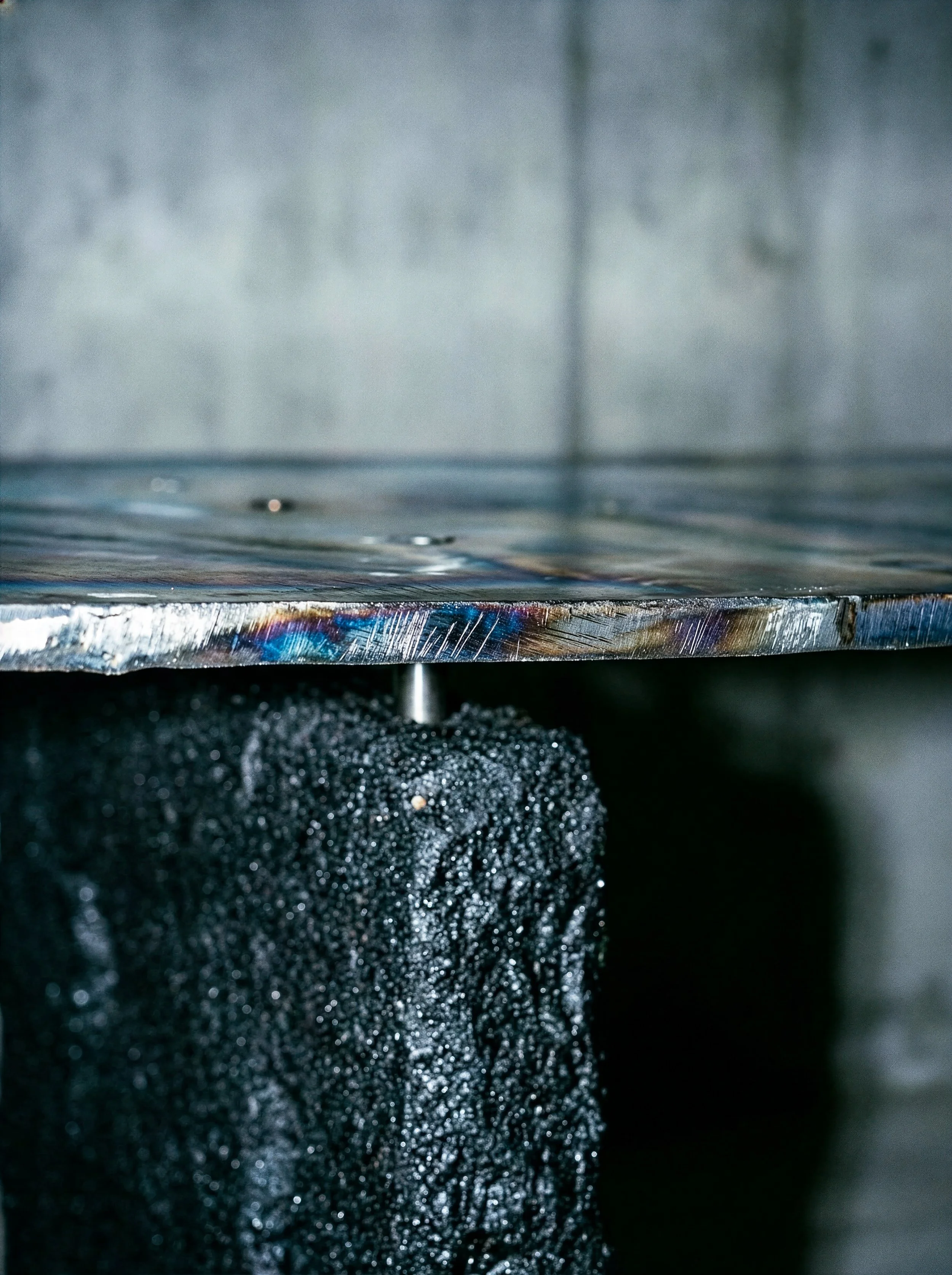 Gros plan d'une table en métal avec un support en béton, la surface de la table est en acier et reflète la lumière.