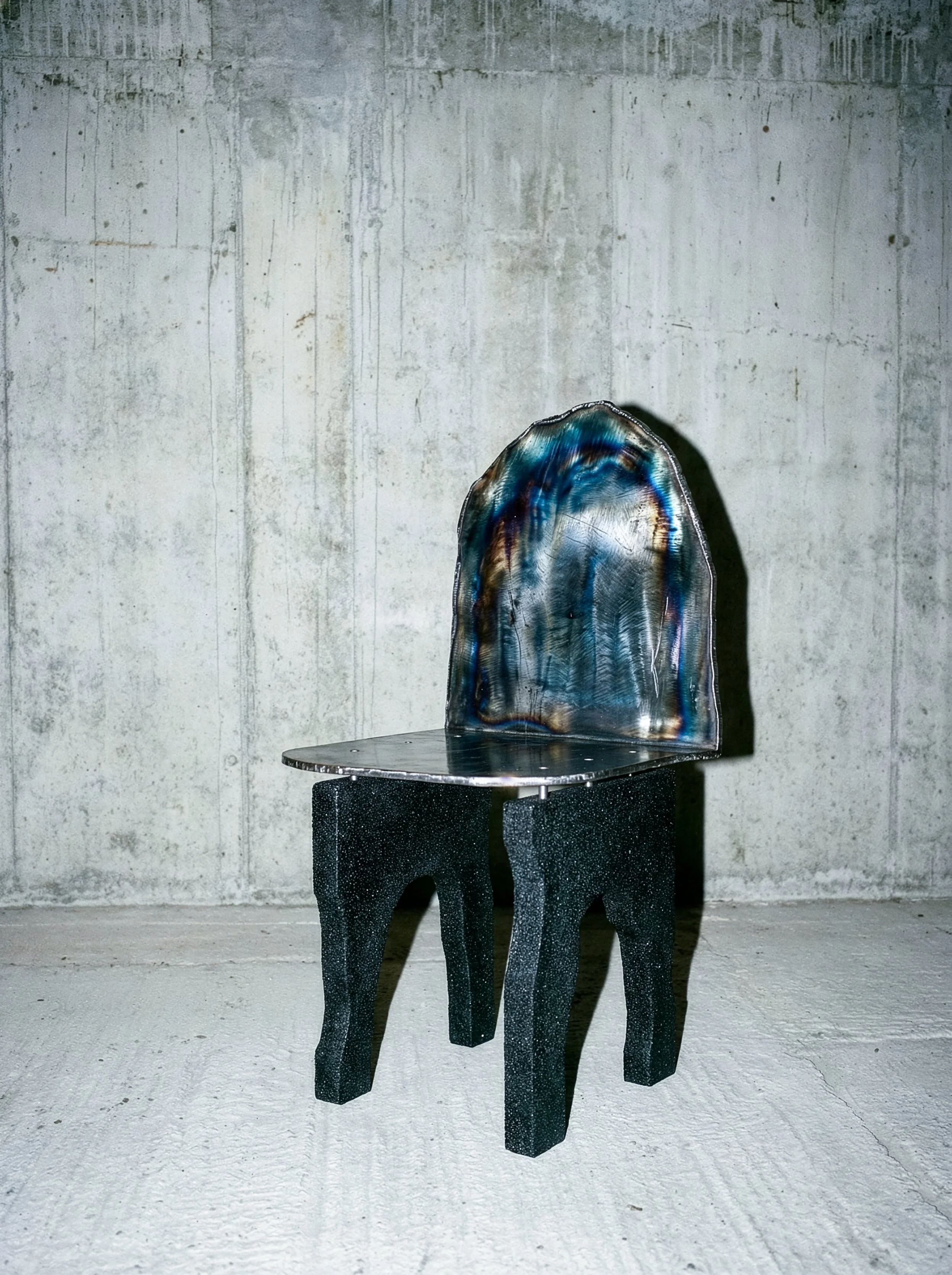 Chaise en métal avec un dossier translucide coloré et une assise noire, placée contre un mur en béton brut. - PAUL HARDY
