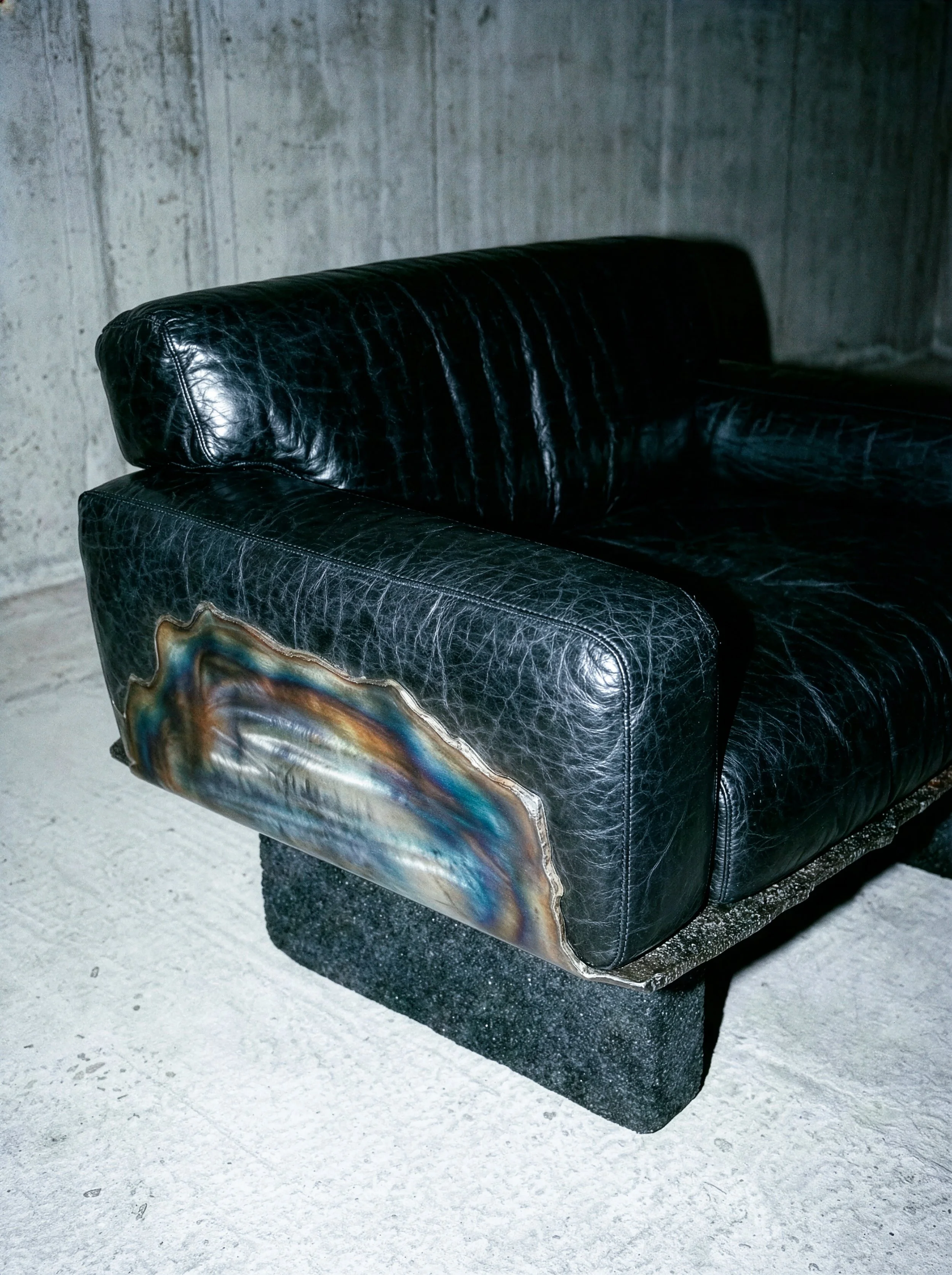 Canapé en cuir noir avec une zone en pierre colorée, dans un espace industriel.  PAUL HARDY