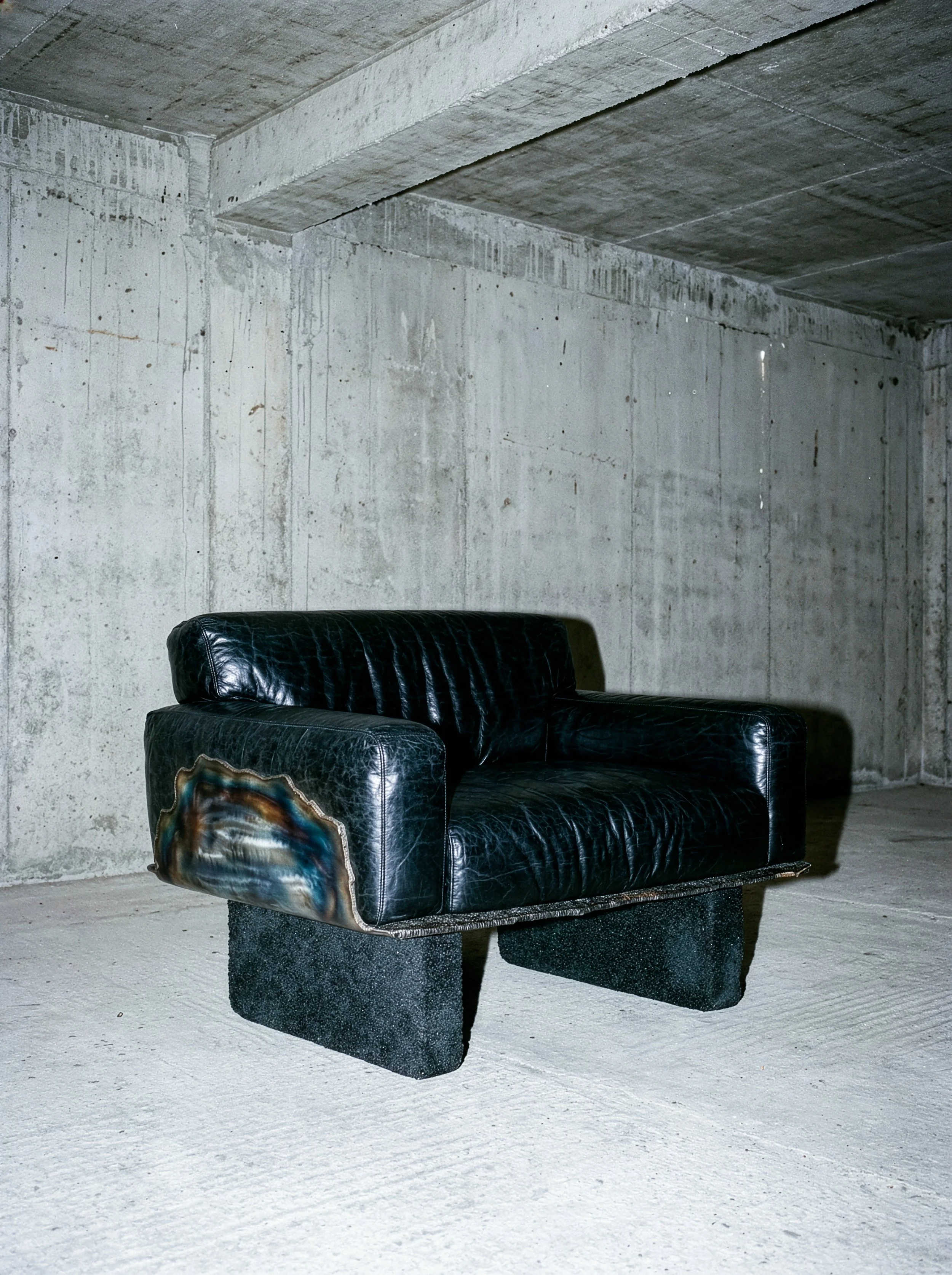 Canapé noir en cuir dans un espace brut avec murs en ciment.  PAUL HARDY