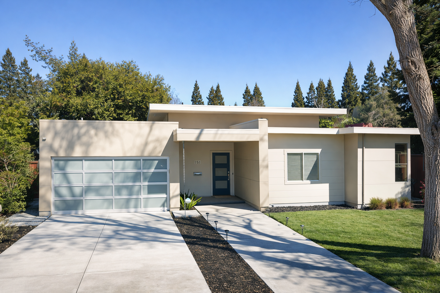 Modern single-story house with a white exterior, glass-paneled garage door, and a small front yard with a sidewalk and grass