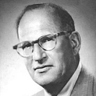 A black and white photo of a man with glasses, short hair, and wearing a suit