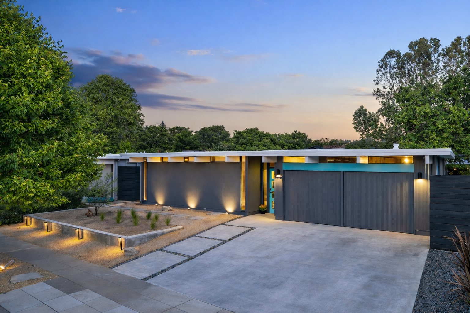 Modern house with clean lines, exterior lighting, surrounded by trees and a landscaped yard at dusk.