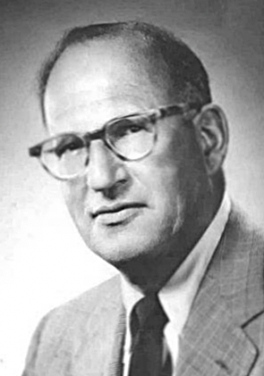 Black and white photo of a middle-aged man with glasses, wearing a suit and tie.