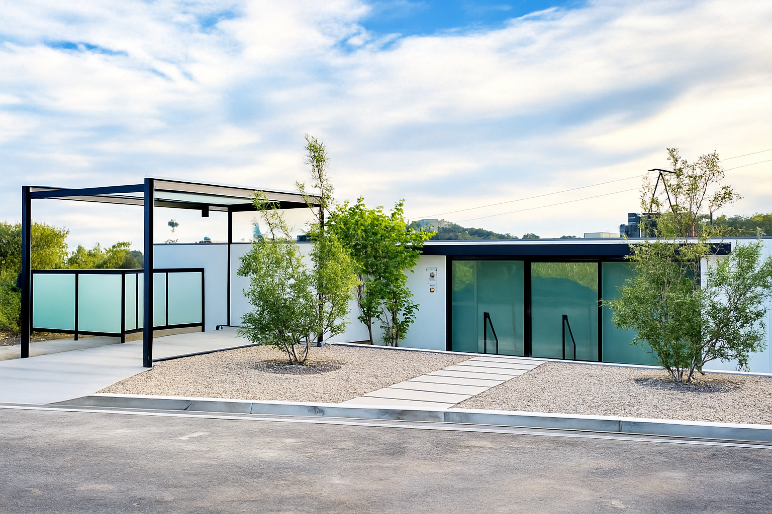 Modern building with glass sliding doors, surrounded by gravel and a few small trees, under a partly cloudy sky