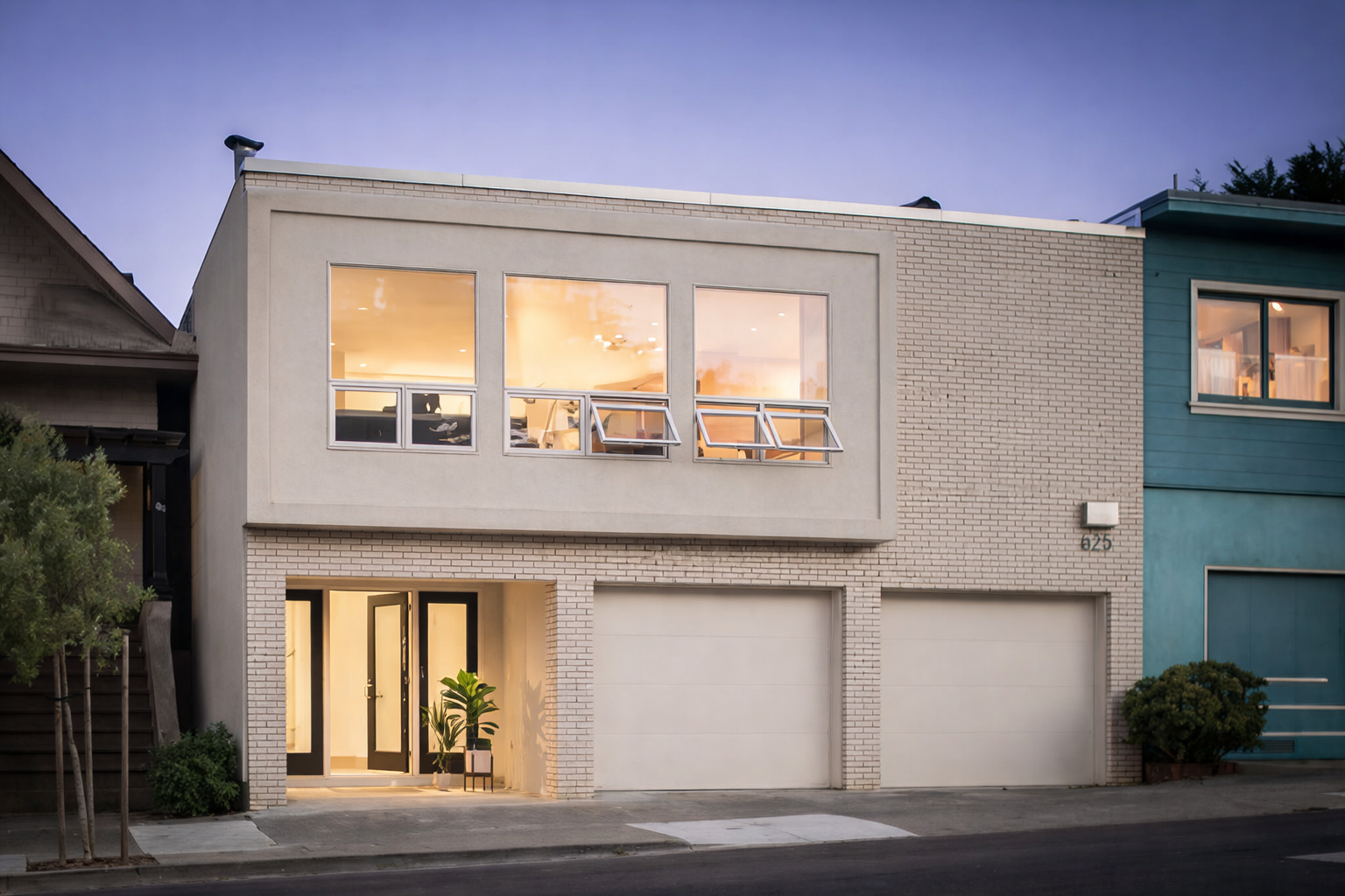 Modern two-story house with white brick and beige stucco exterior, large front windows, glass front door, and a garage; plants near entrance; house number 625; situated on a city street during twilight.