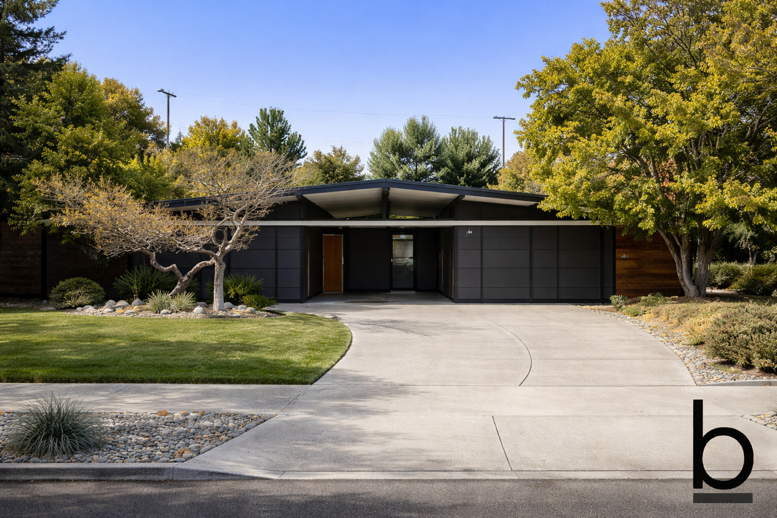Modern single-story house with black exterior, front driveway, and landscaping including trees and shrubs, under a clear blue sky.