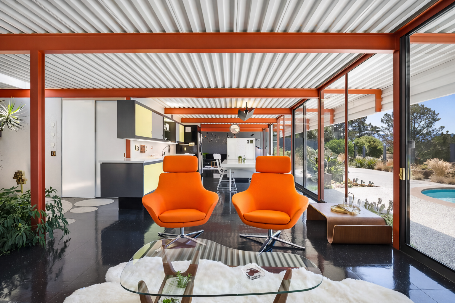 Modern living room with bright orange chairs, a glass coffee table, large windows with a view of a backyard with a pool and desert landscaping, and a kitchen in the background.