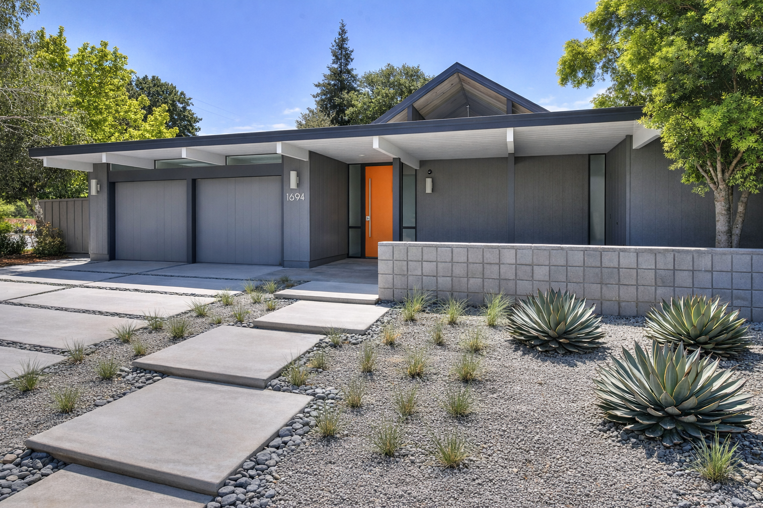 Modern house with a gray facade, orange front door, and a minimalist yard with concrete stepping stones, rocks, and drought-tolerant plants.