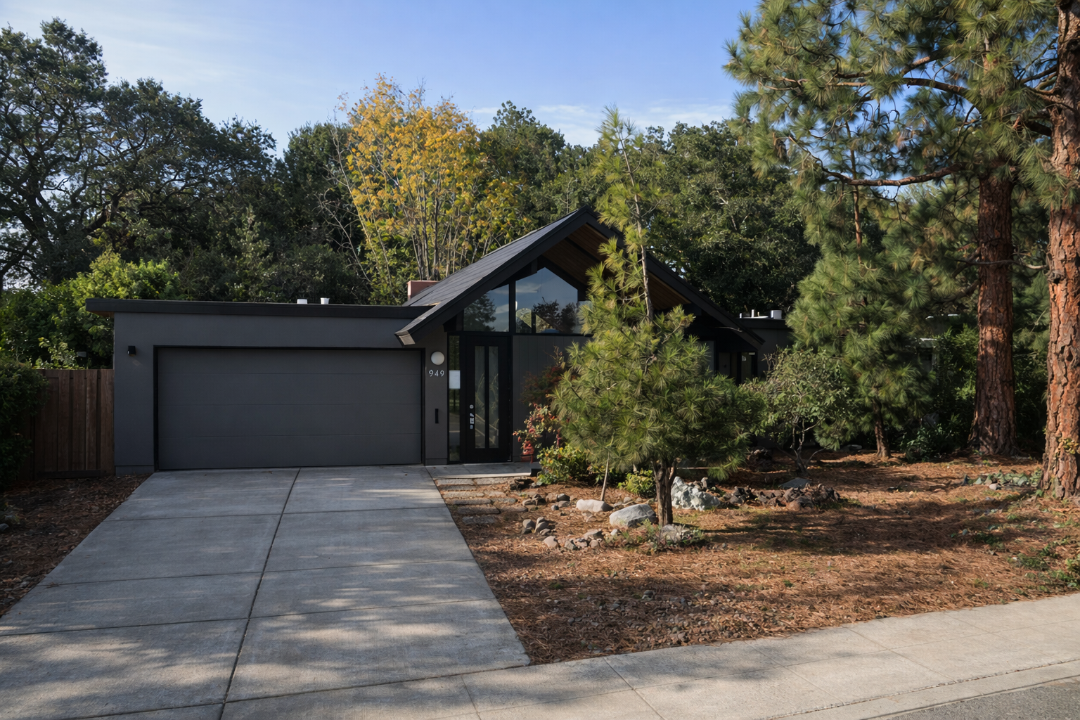 Modern house with a black exterior, adjacent driveway, and surrounded by trees and shrubs, located on a residential street.