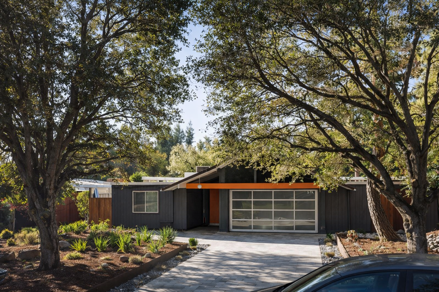 Front view of a modern house with a dark exterior, large garage door, surrounded by trees and landscaping.