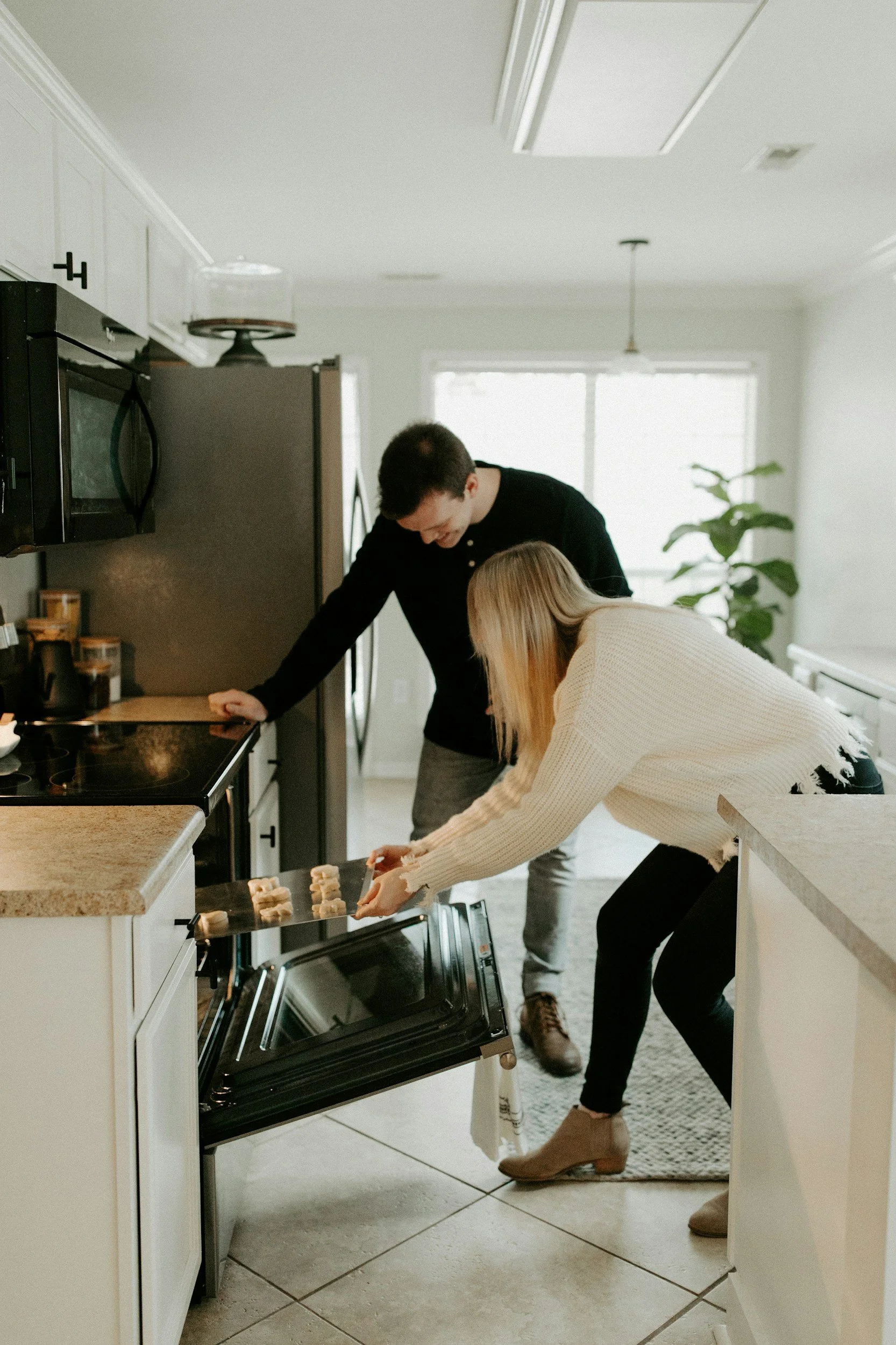 A woman placing cookies on the oven rack while a man stands nearby in a kitchen.