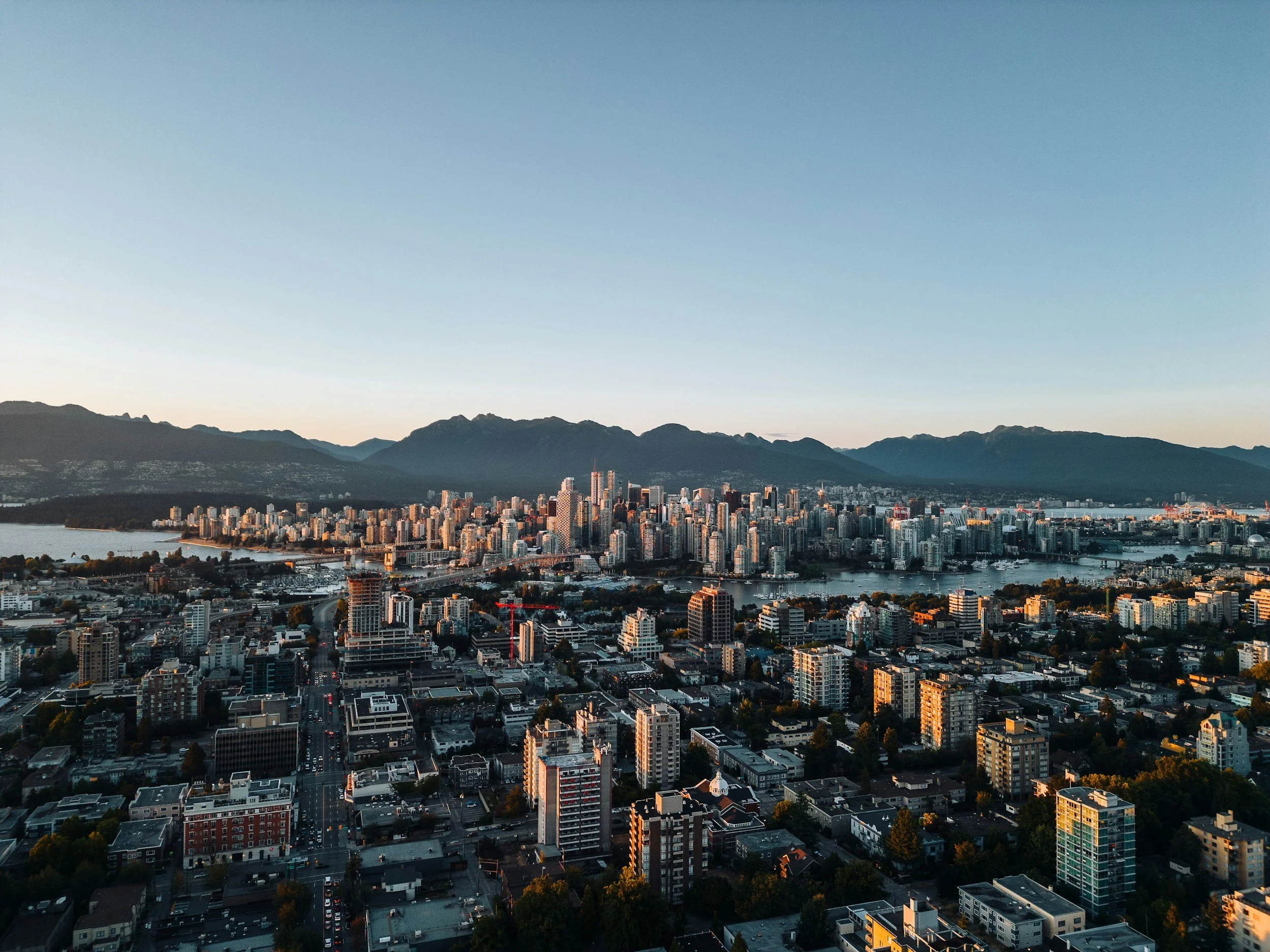 Cityscape of Seattle with tall buildings, Lake Union, and surrounding mountains at sunset.