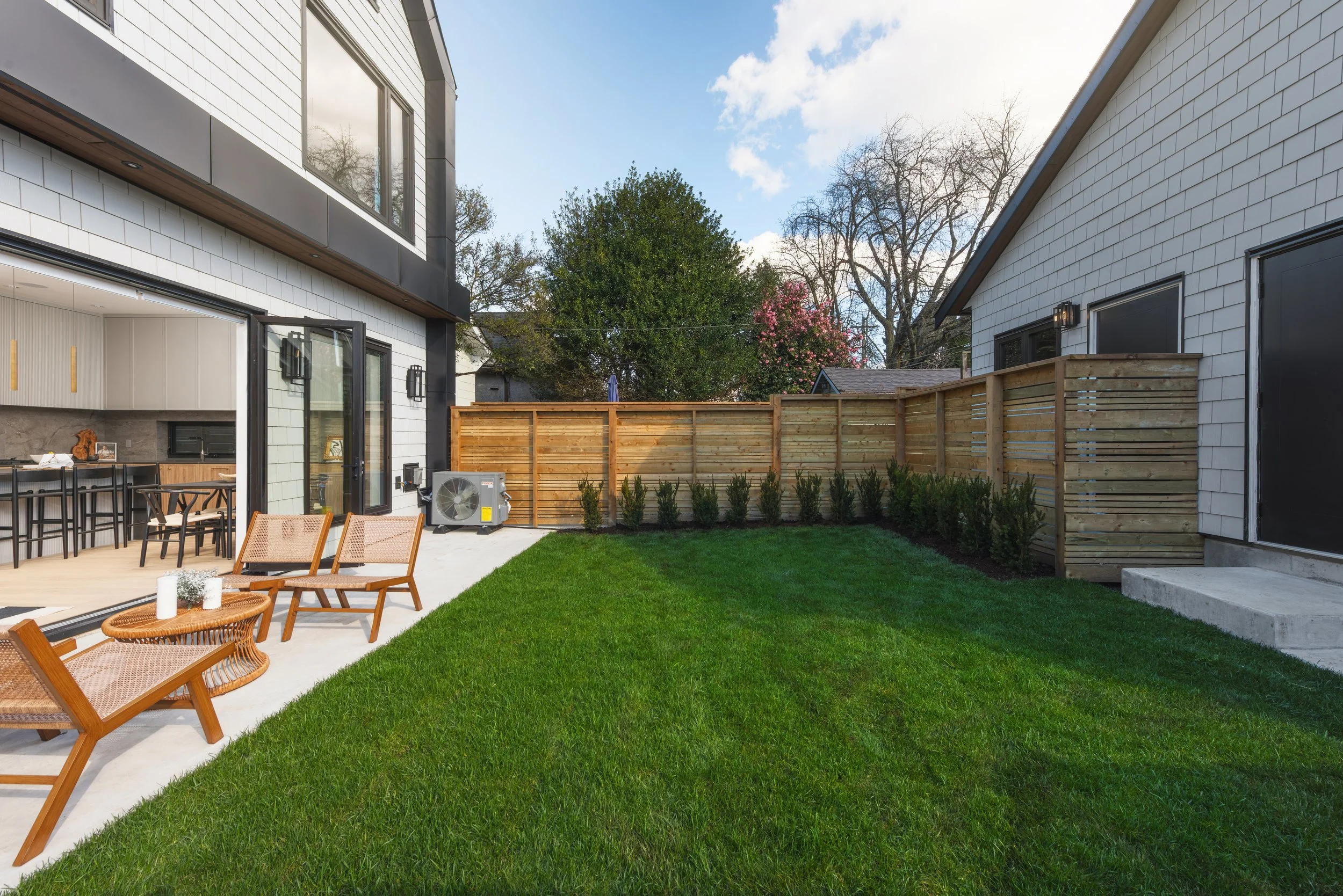 A modern backyard with a green lawn, outdoor seating, and a wooden privacy fence, adjacent to a house with sliding glass doors leading inside.