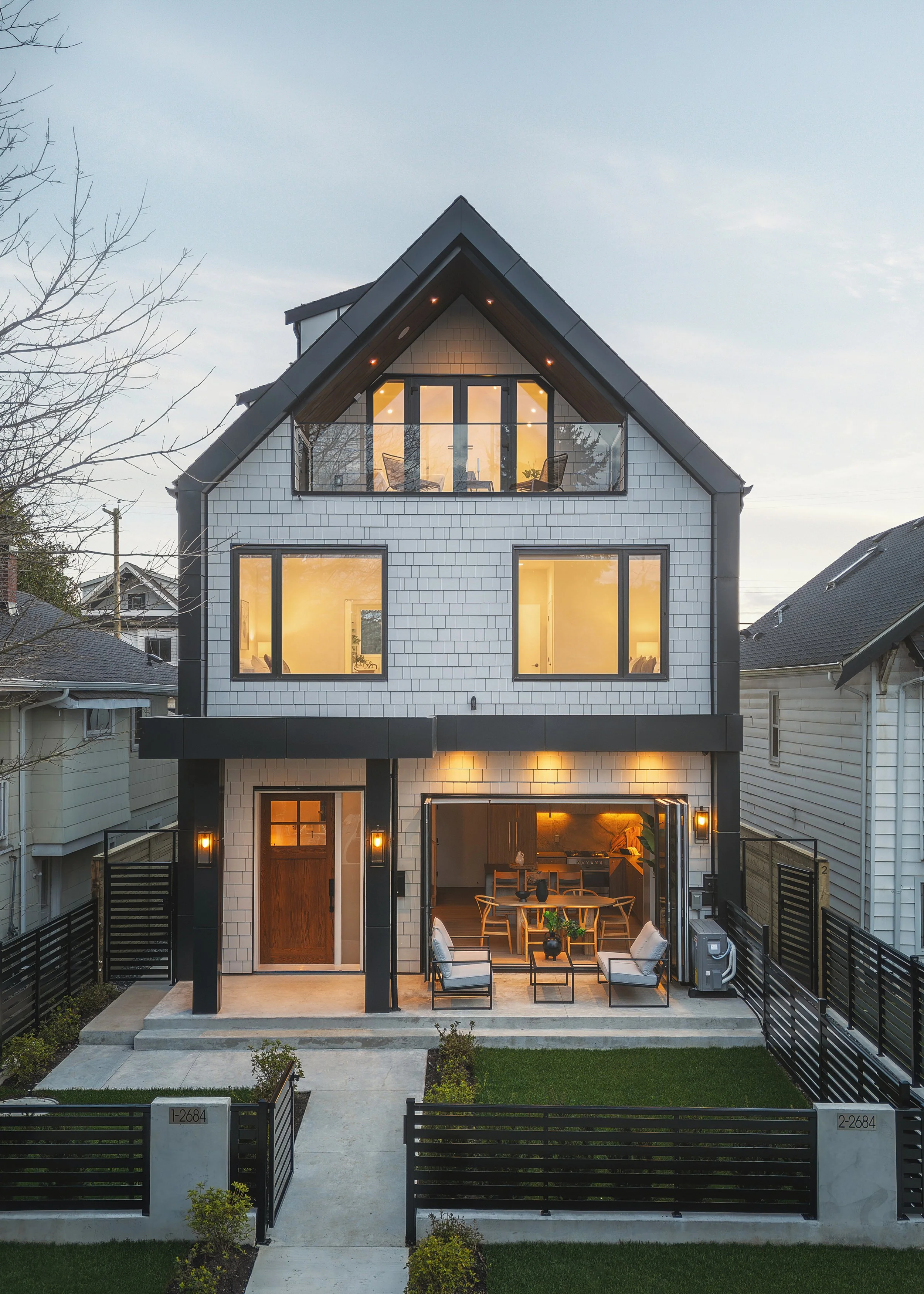 Modern three-story house with large windows, a garage, and a small front yard with a walkway and black fence.