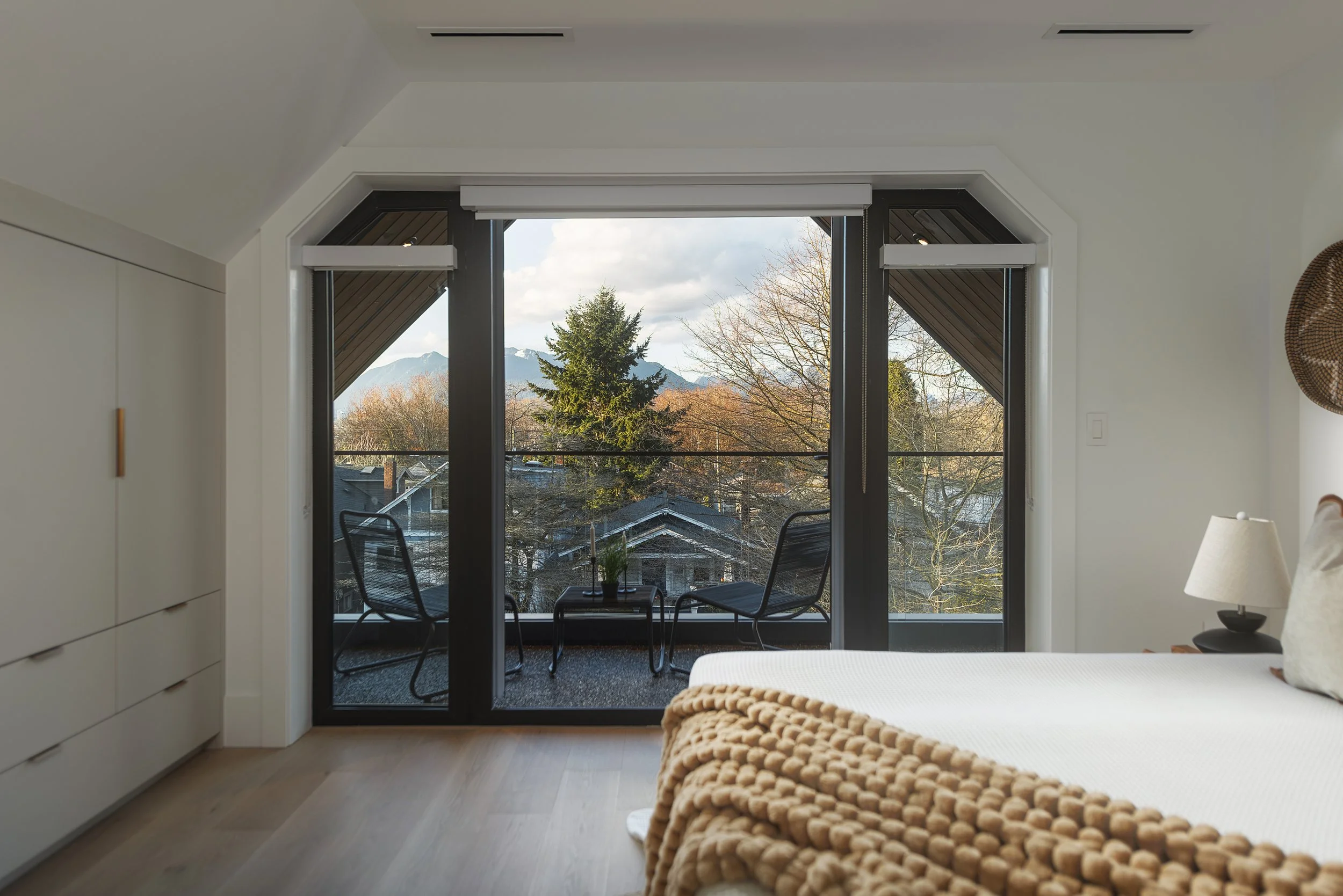 Bedroom with large glass sliding door leading to balcony overlooking trees and mountains in the distance.
