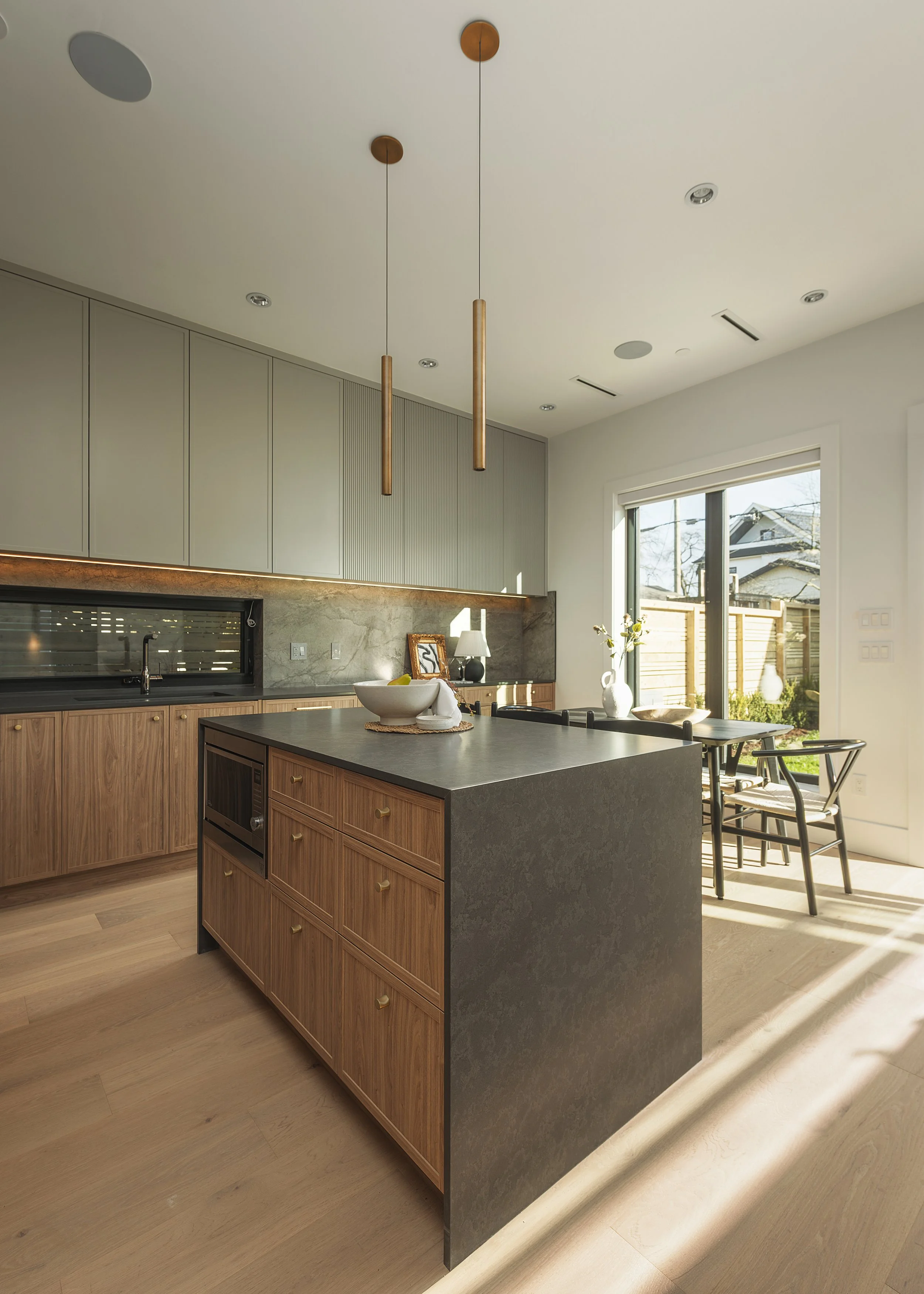Modern kitchen with a center island, wooden cabinets, minimalist decor, and large sliding glass doors leading to a backyard.