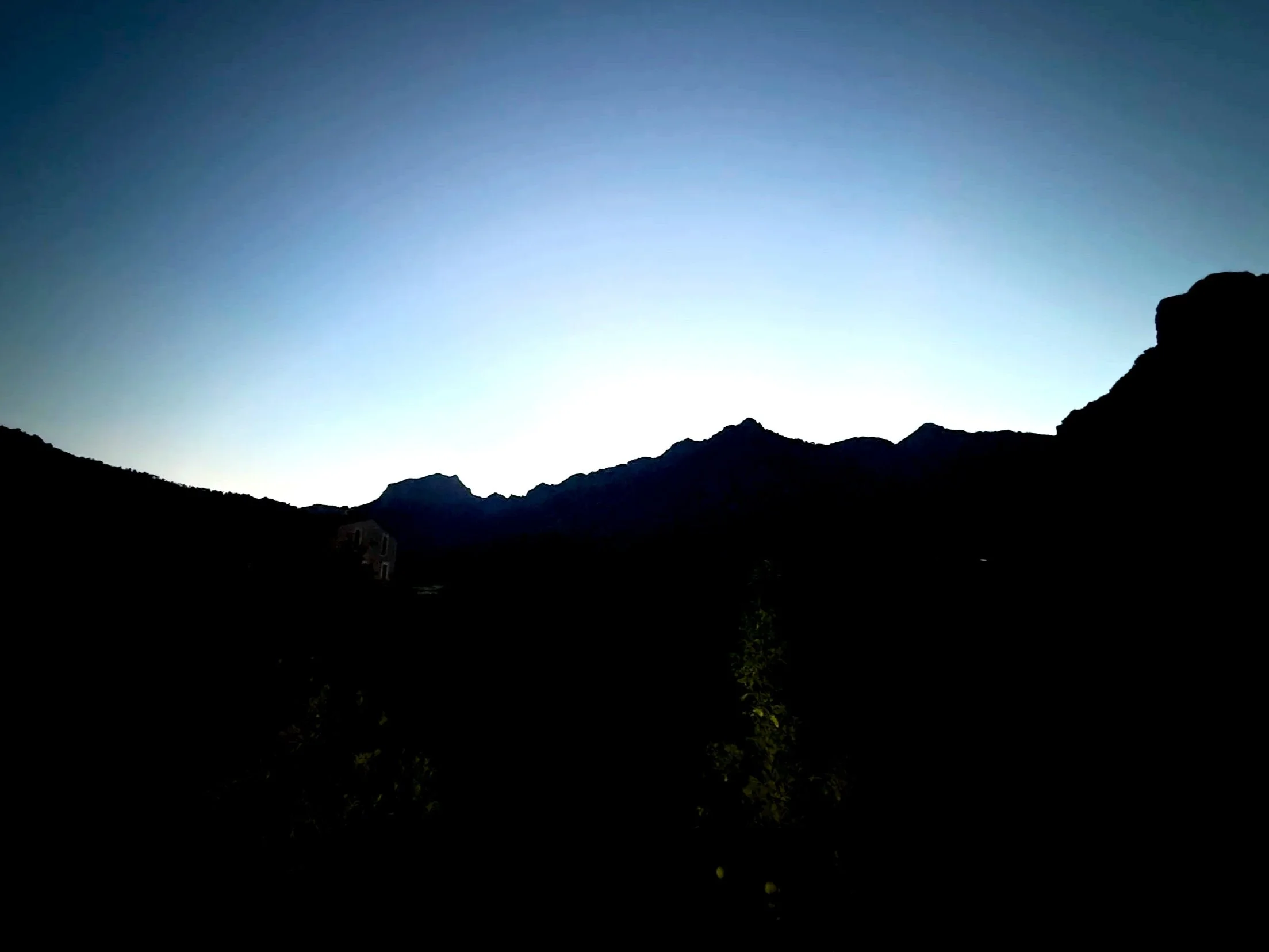 Silhouette of mountains against a blue sky at dawn.