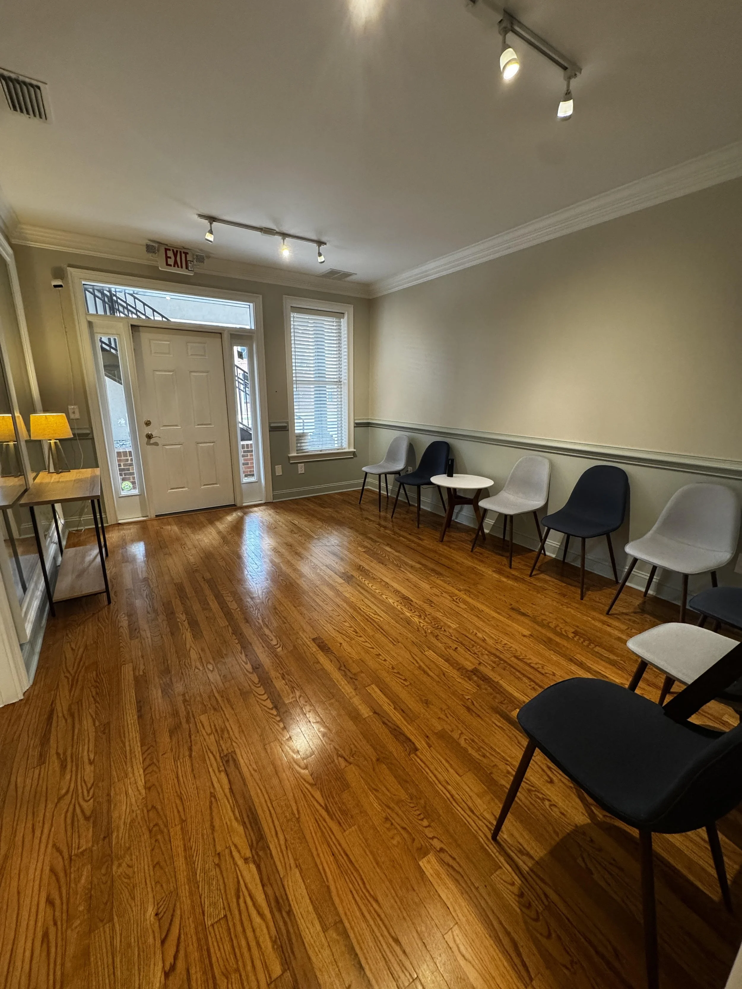 A picture of the lobby of In-Focus: Relational Therapy. It features dark and light blue chairs, warm wood floors and calming beige and light green wall paint.