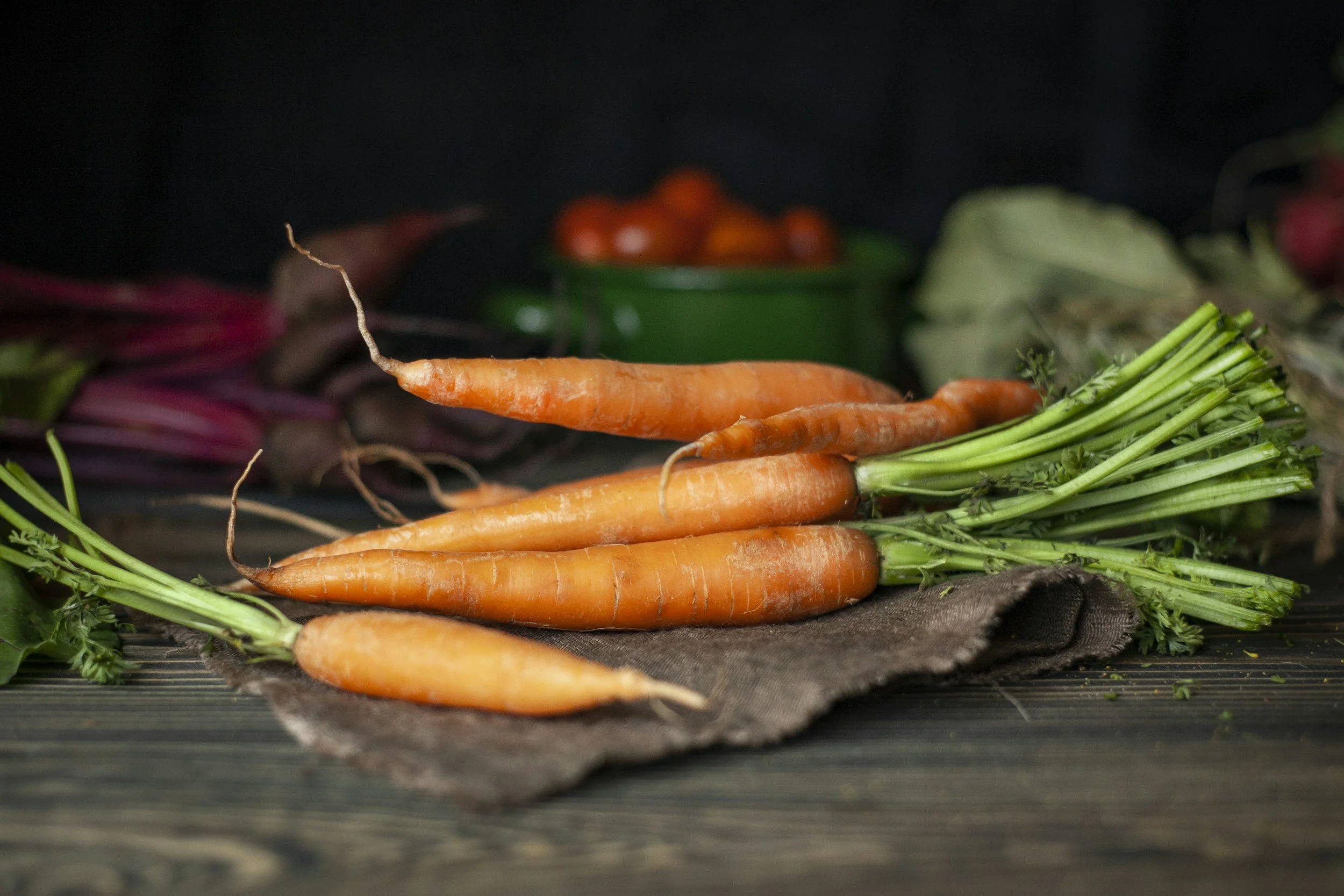 Fresh orange carrots with green tops lying on a dark wooden surface with a black background.
