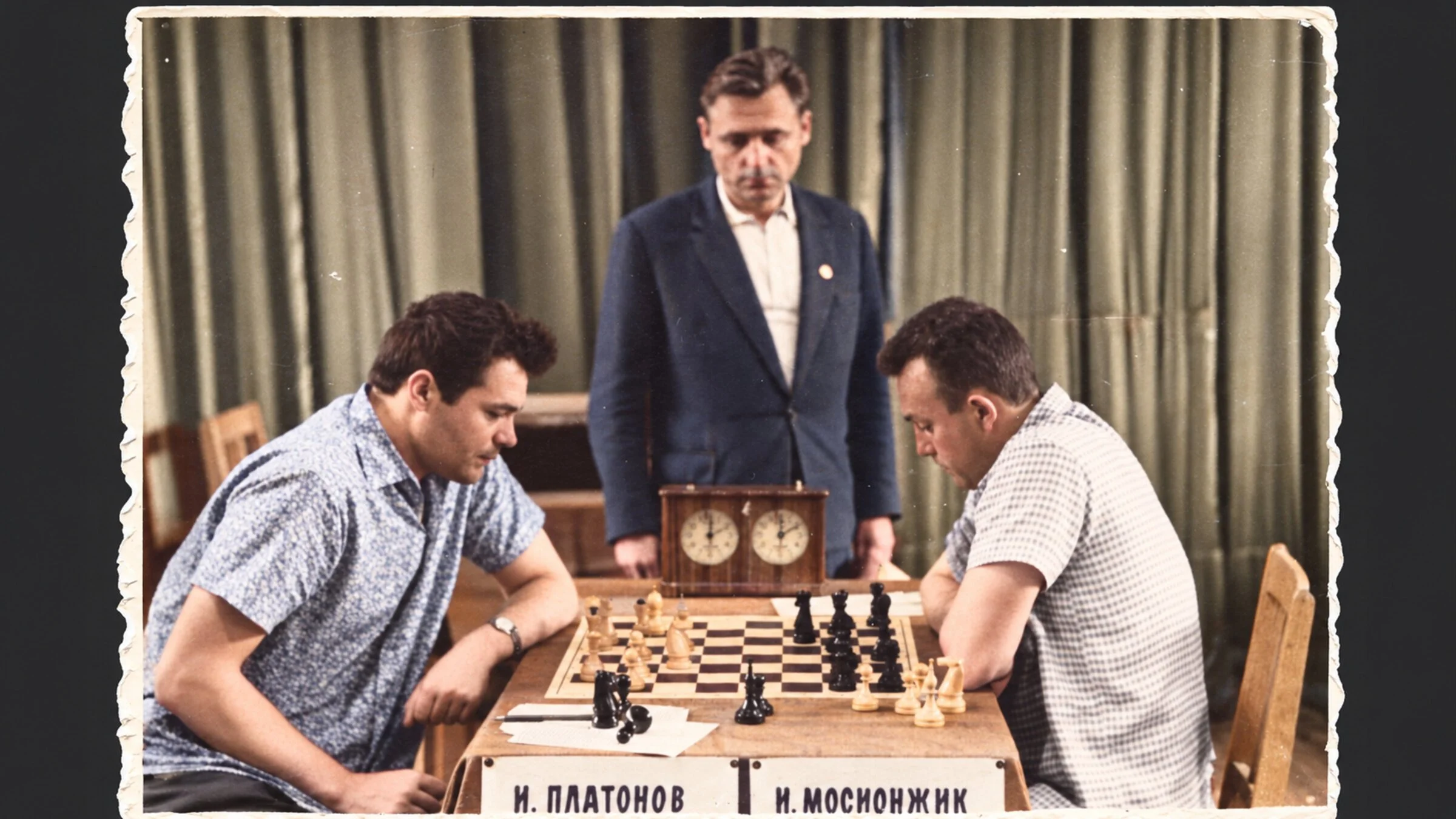 Colorized photograph of Igor Platonov, left, playing I. Mosionzhik in the 1960s, with an observer standing behind the chessboard.