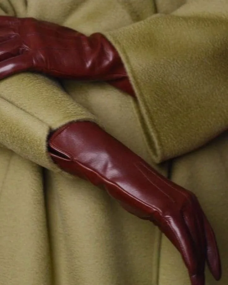 Une main gantée de rouge ressort d'une veste beige en laine.