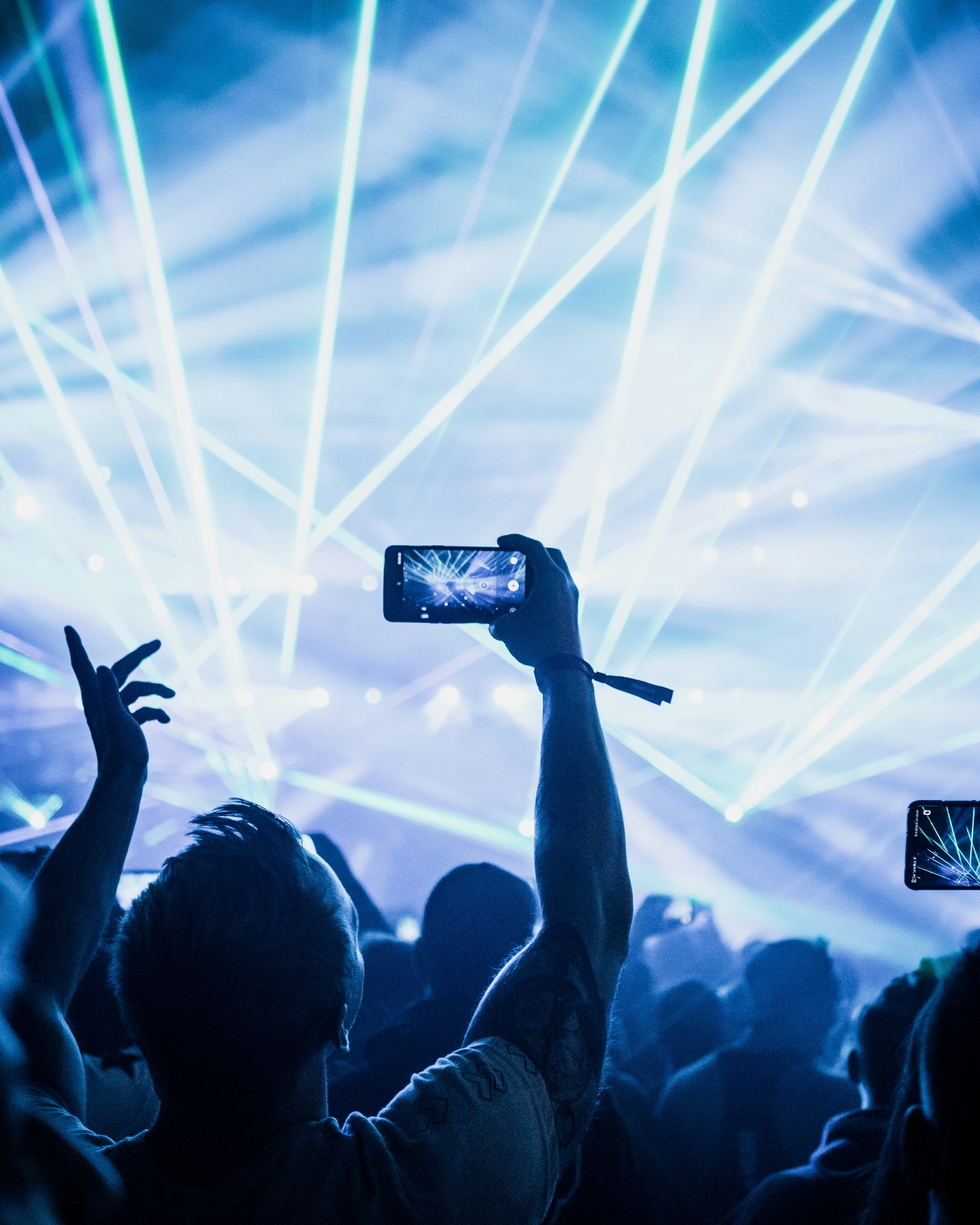 Concert scene with an audience taking photos of a stage with laser lights.
