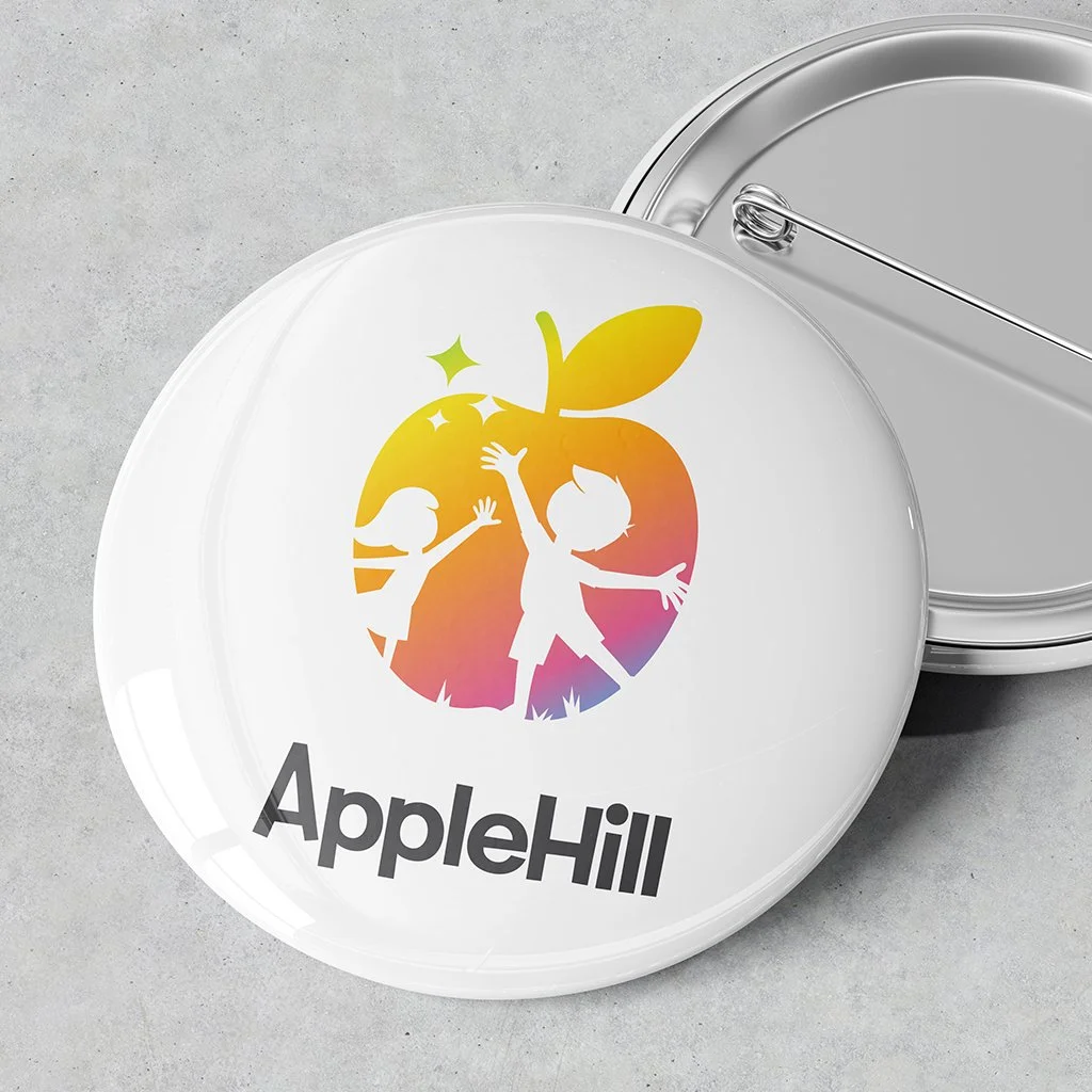 A white round object with the Apple Hill logo featuring a colorful apple and two children reaching up, and the text 'Apple Hill' below.