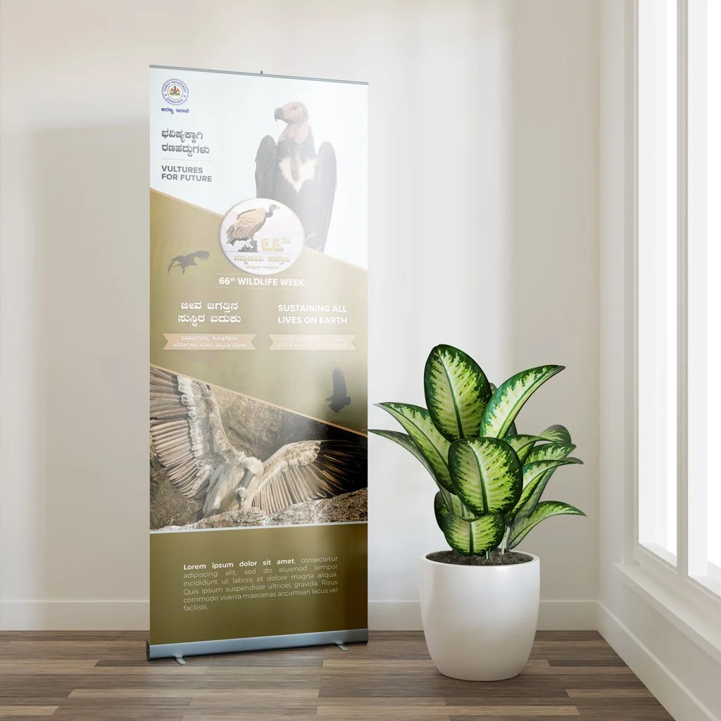 A vertical banner for wildlife week featuring a vulture, a silhouette of a flying bird, and a bird in flight, with text in English and Kannada, placed next to a potted green plant near a window.