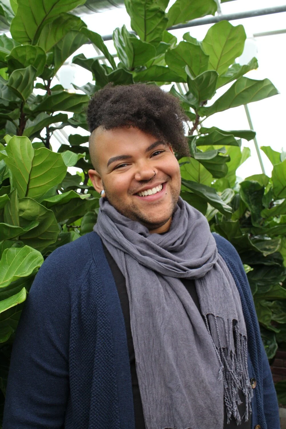 picture of Cavanaugh Quick, an Afro-latine nonbinary person with side-cut and long tight curls, wearing blue-grey scarf