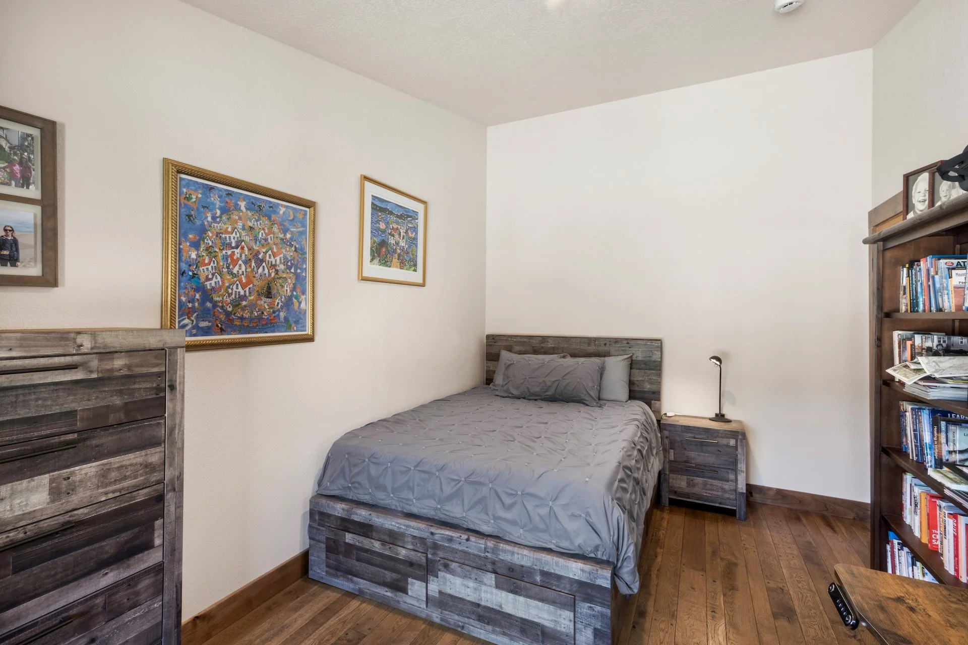 Bedroom with a rustic wooden bed, nightstand, bookshelf, and framed artwork on the walls.